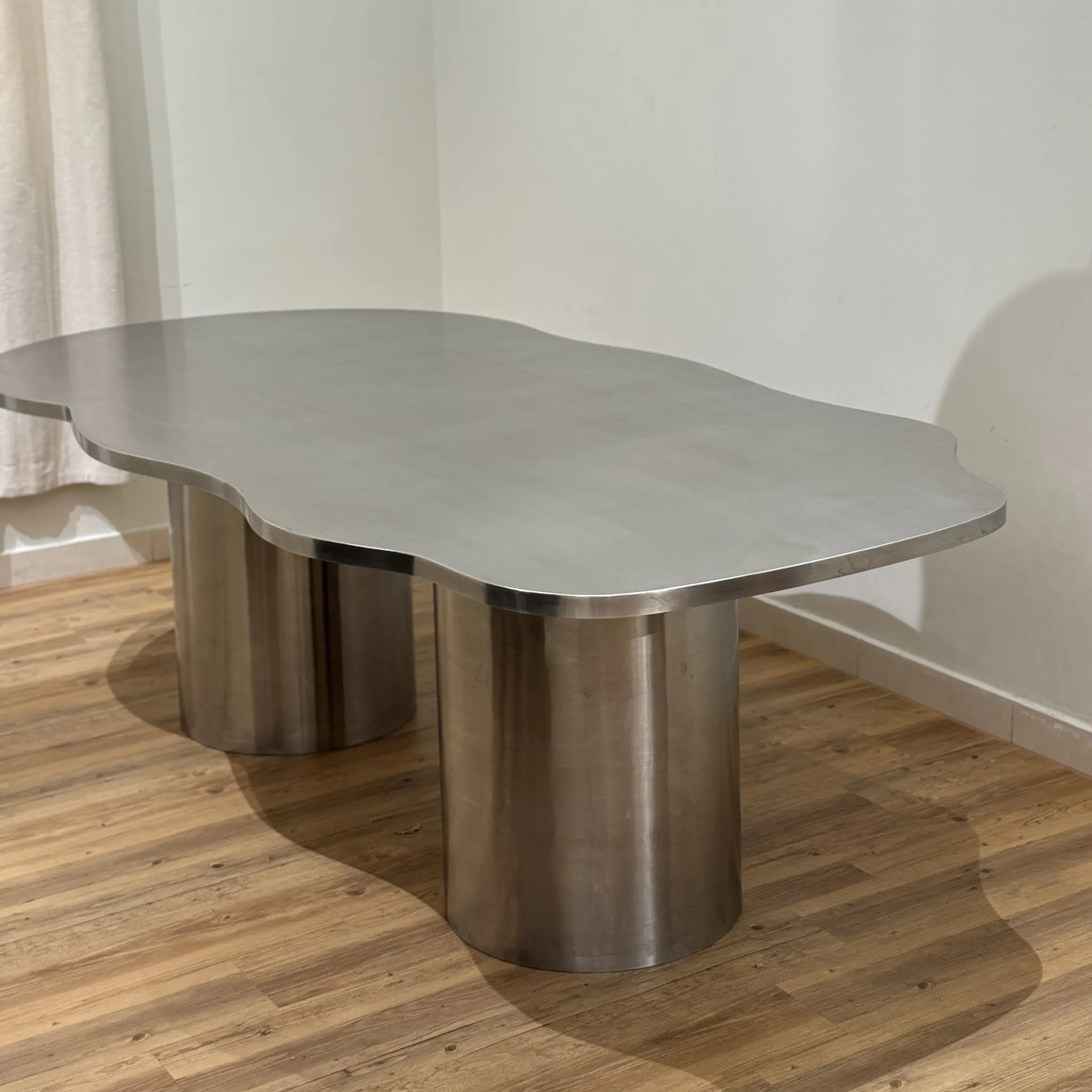 Stylish steel dining table with a reflective stainless steel top, placed in a spacious and chic dining area.