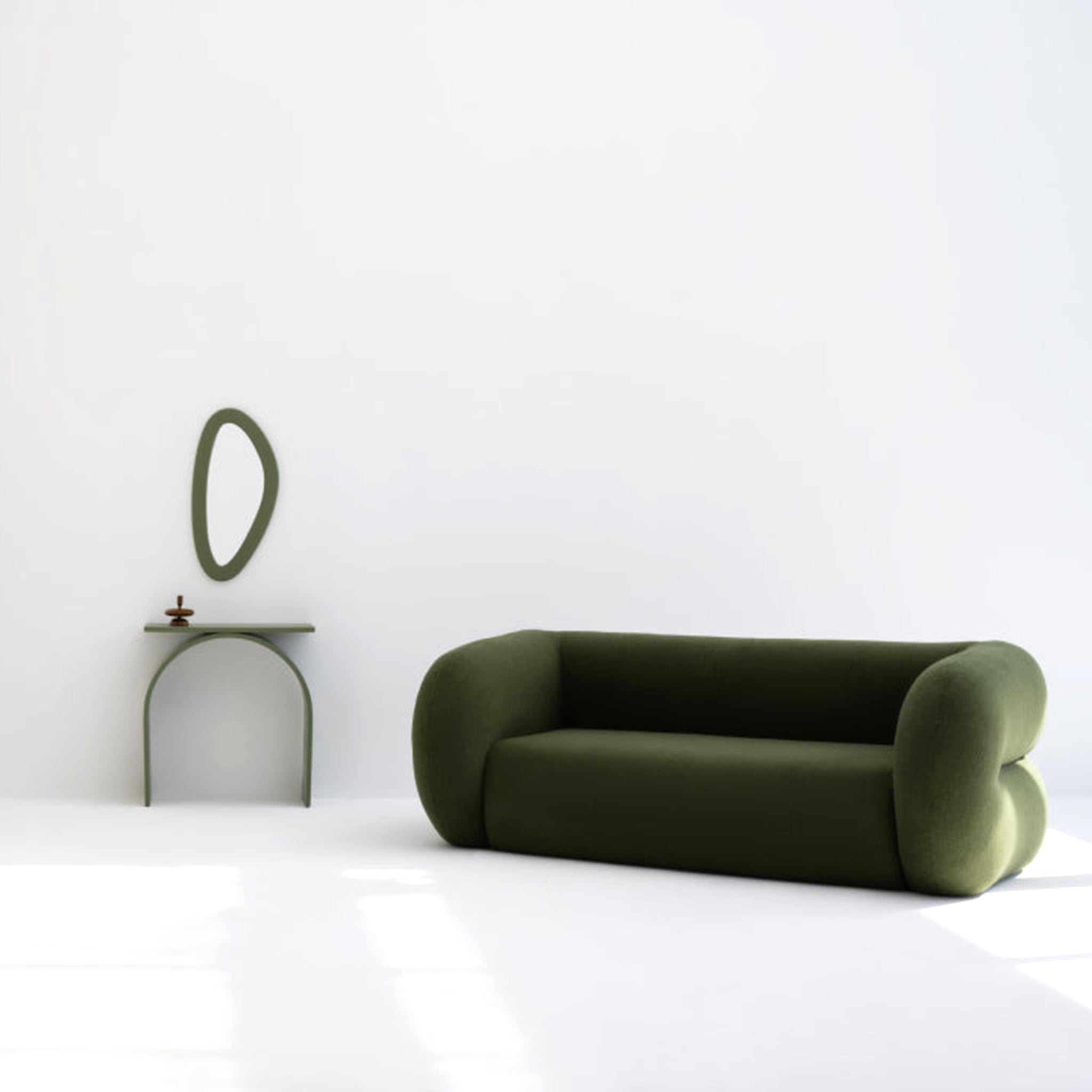 Minimalist living room with a modern green sofa featuring soft, rounded edges, accompanied by a matching side table and a unique oval mirror on a white wall.
