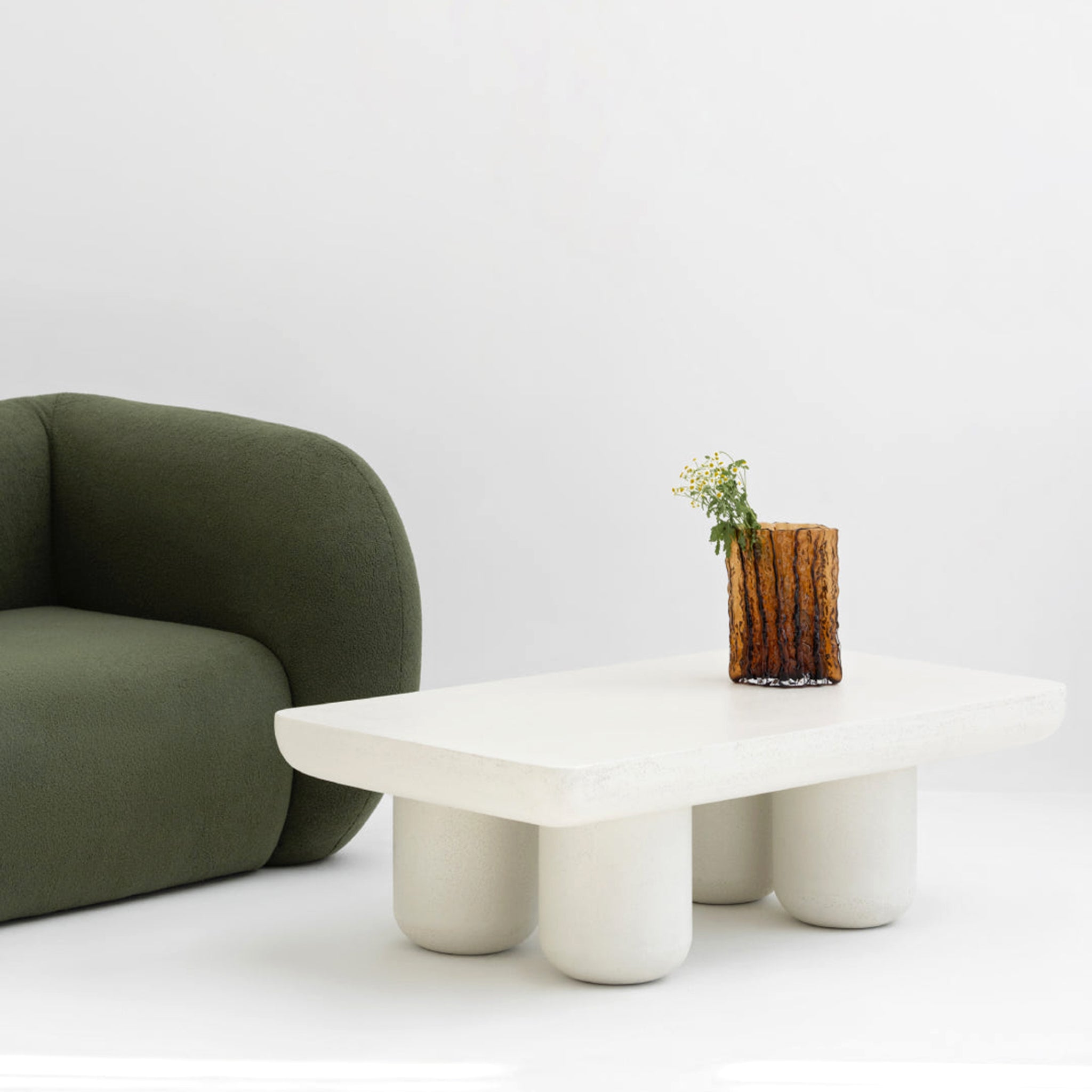 Minimalist interior with a modern green sofa and a unique white coffee table, adorned with a decorative vase and fresh flowers.buy a modern seating sofa