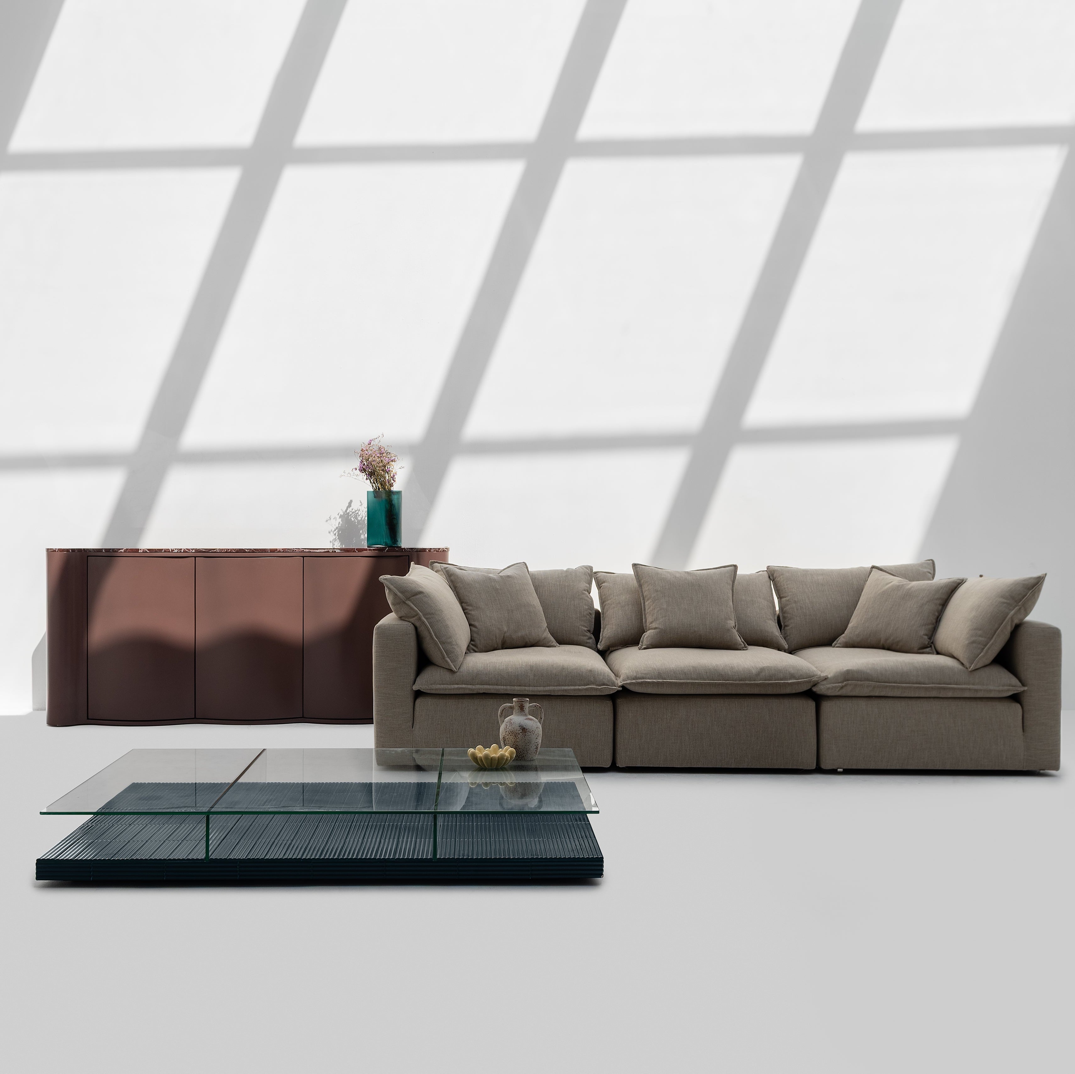 Modern living room with a gray sectional sofa, glass coffee table, and wooden sideboard.
