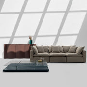Modern living room with a gray sectional sofa, glass coffee table, and wooden sideboard.