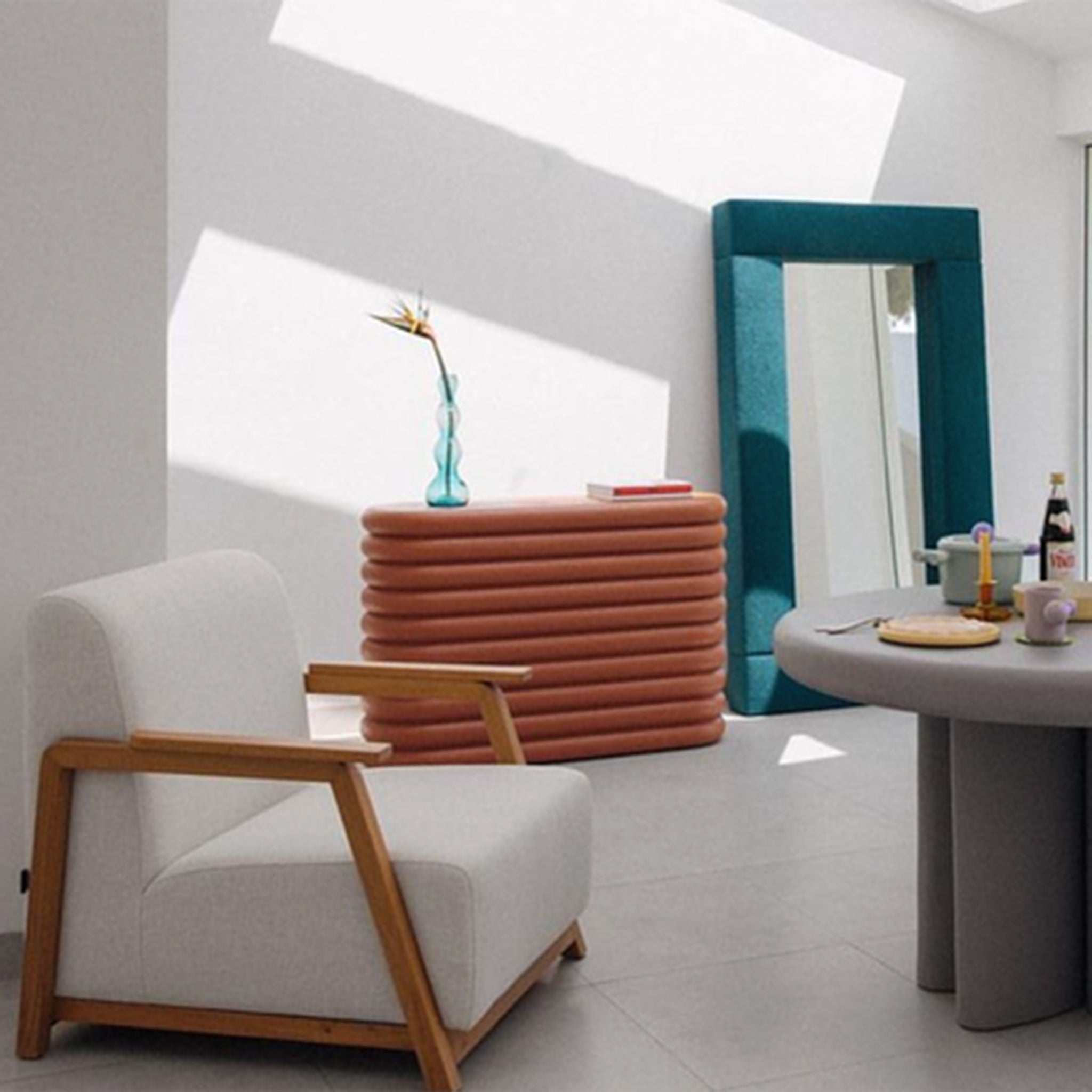 "Contemporary living room featuring a modern console table with a terracotta microplaster finish, a sleek armchair with wooden arms, and a stylish teal mirror, all bathed in natural light."