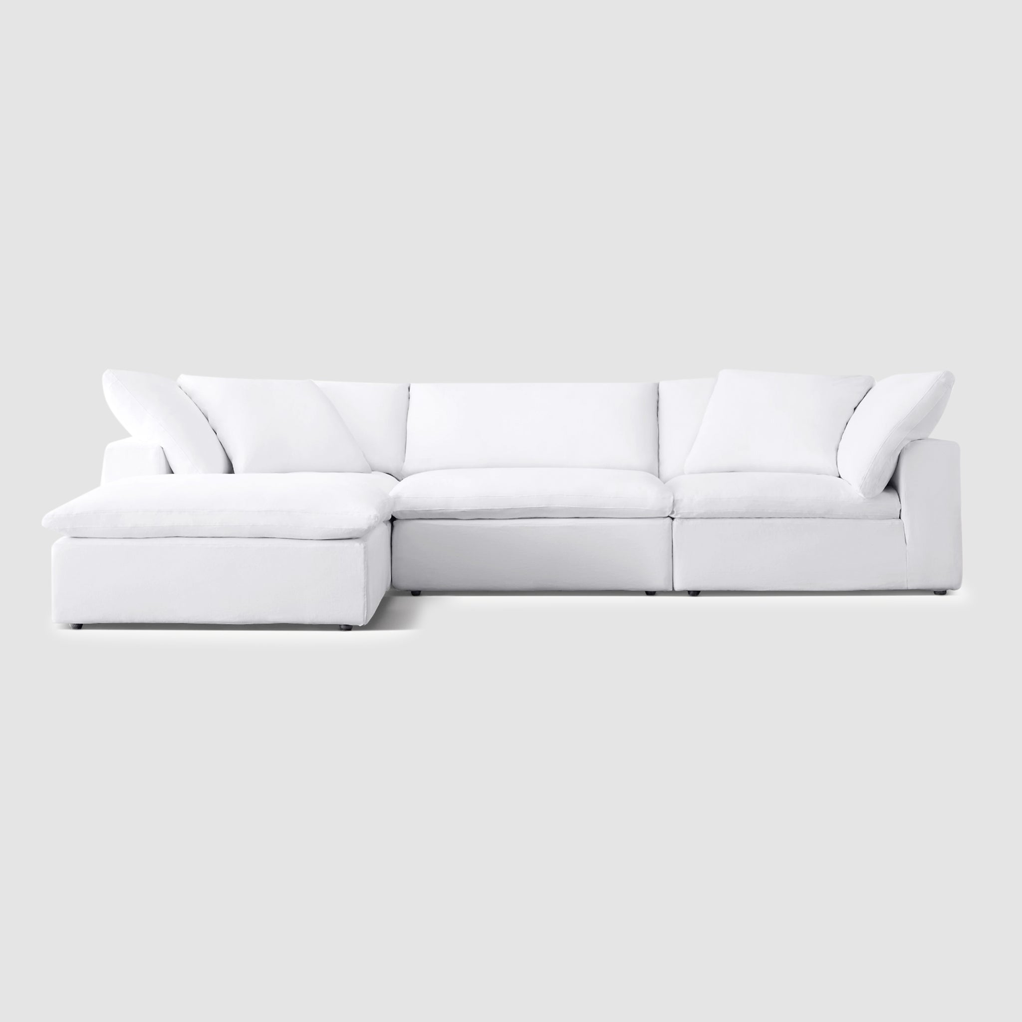 White sectional couch with detachable ottoman in a modern living room. The couch has soft, cloud-like cushions and a solid wood frame.