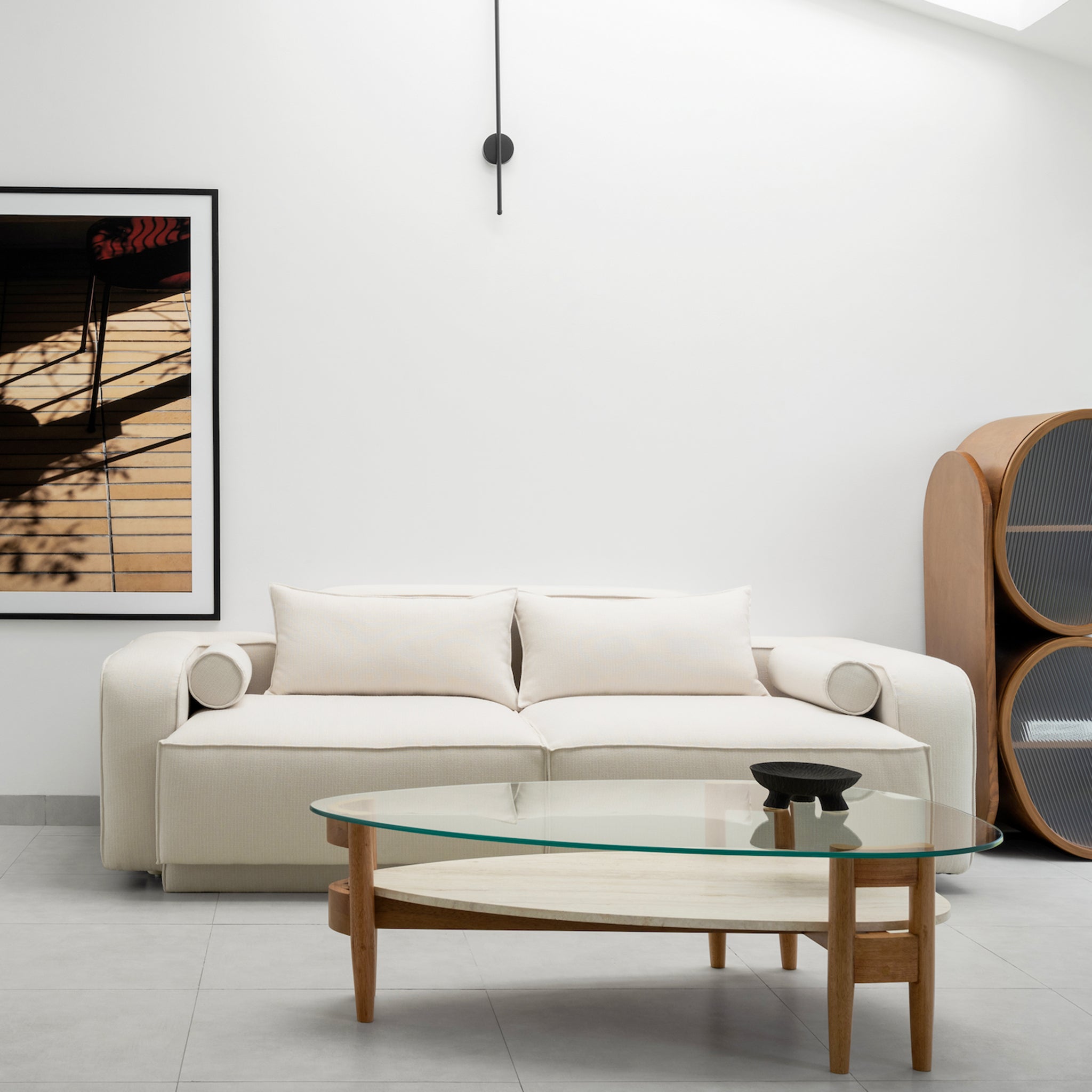 Mid-century modern living room with a white sectional sofa, brown leather ottoman, and round wood and black metal side table with lamp for a touch of sophistication.