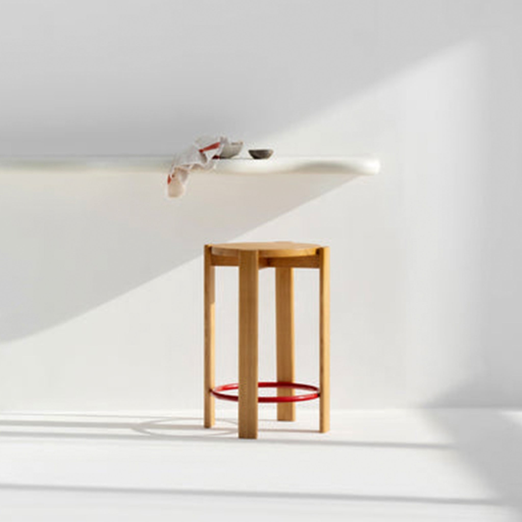Wooden bar stool with a red circular footrest placed in a bright, minimalist kitchen