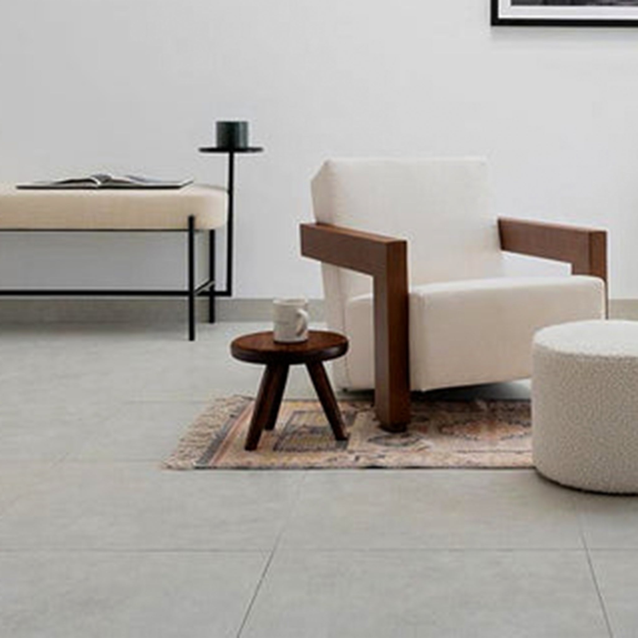 Modern living room with a white armchair, a wooden mini stool with a cup, a round pouf, and a minimalist bench