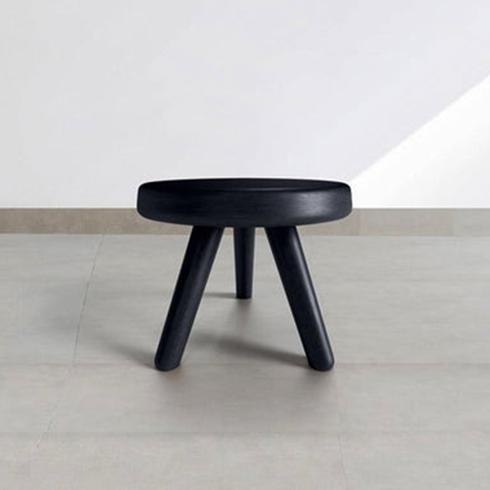 Black wooden mini stool with three legs in a minimalist room