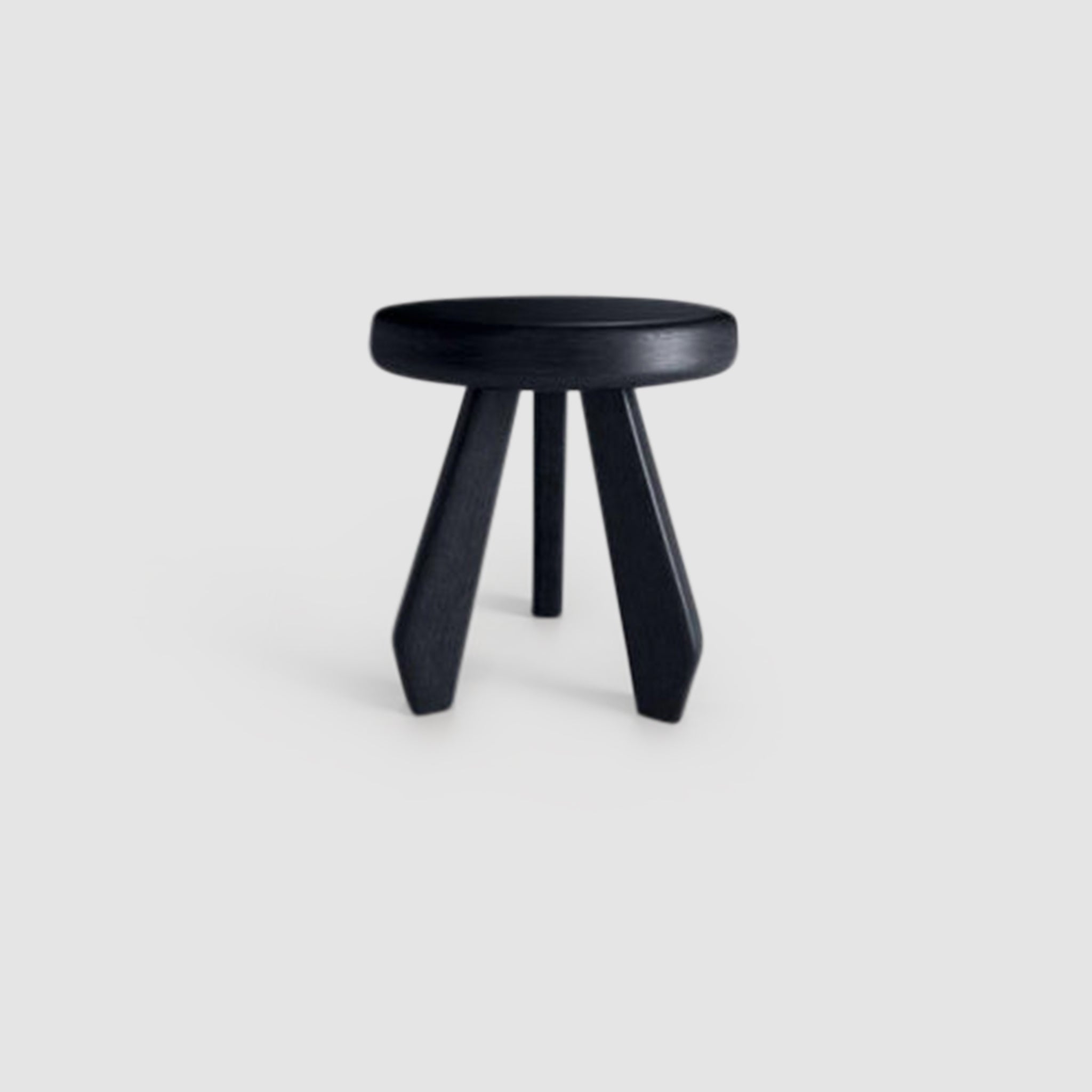 Black wooden three-legged stool with a round seat and tapered legs on a white background