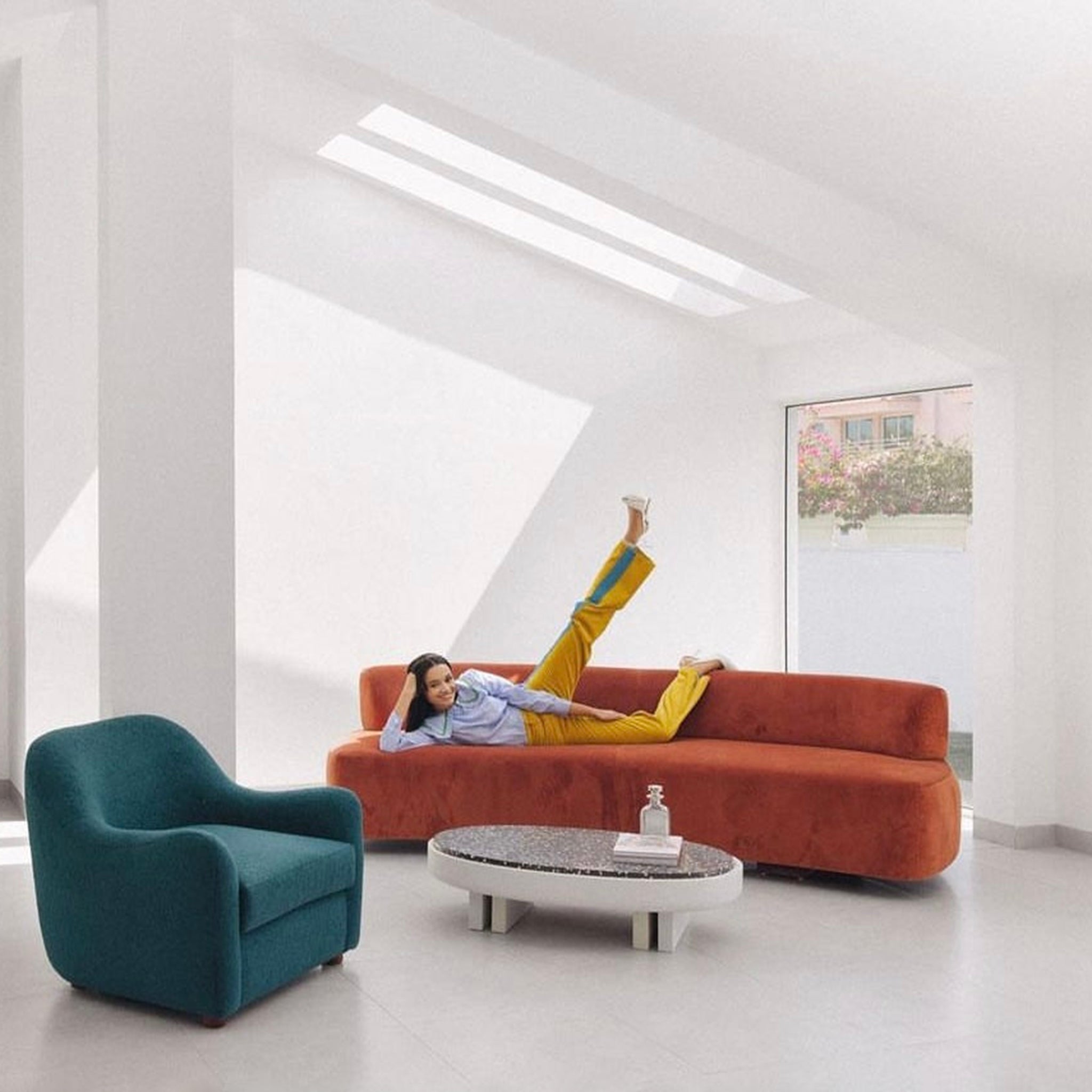 Bright and airy living room with a woman relaxing on a contemporary orange couch