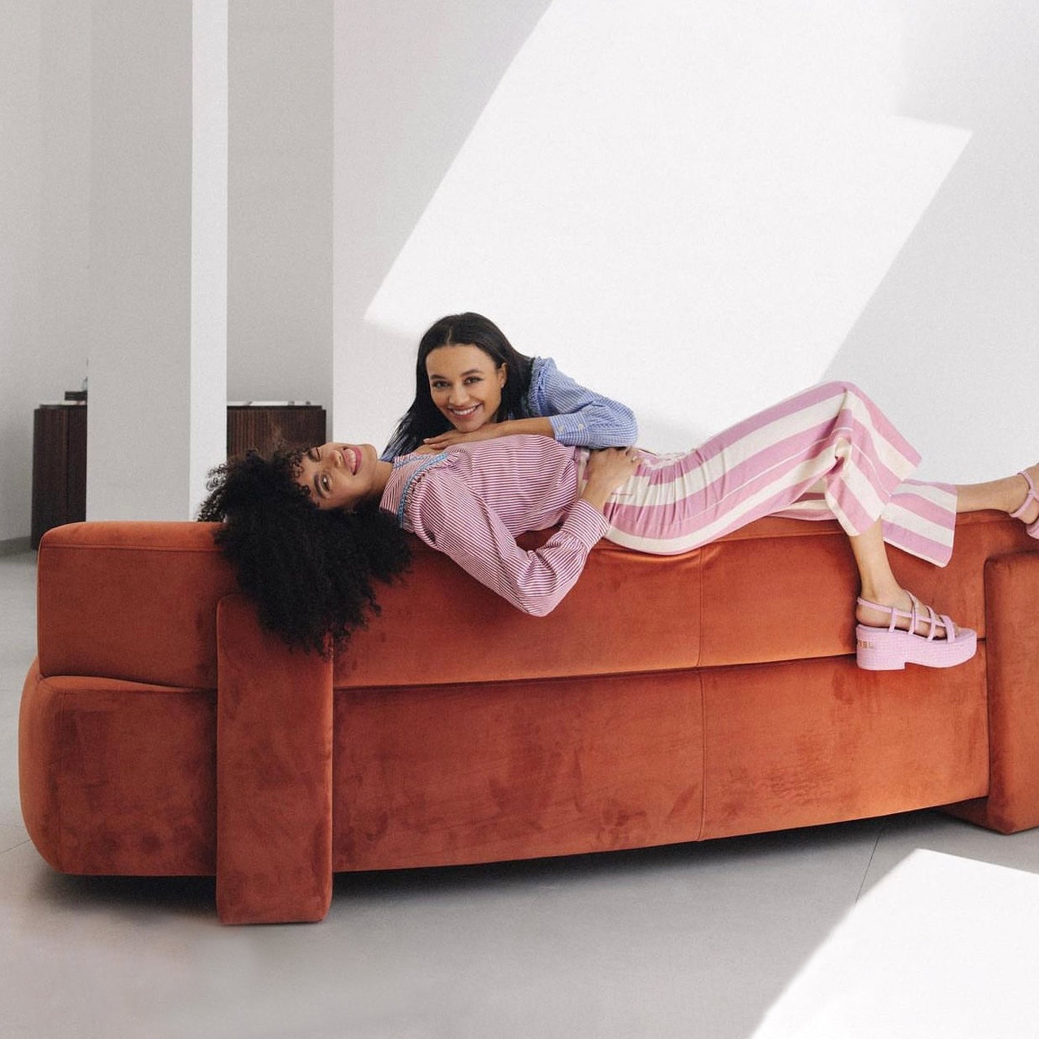 Two women laughing and lounging on an orange sofa in a modern living room