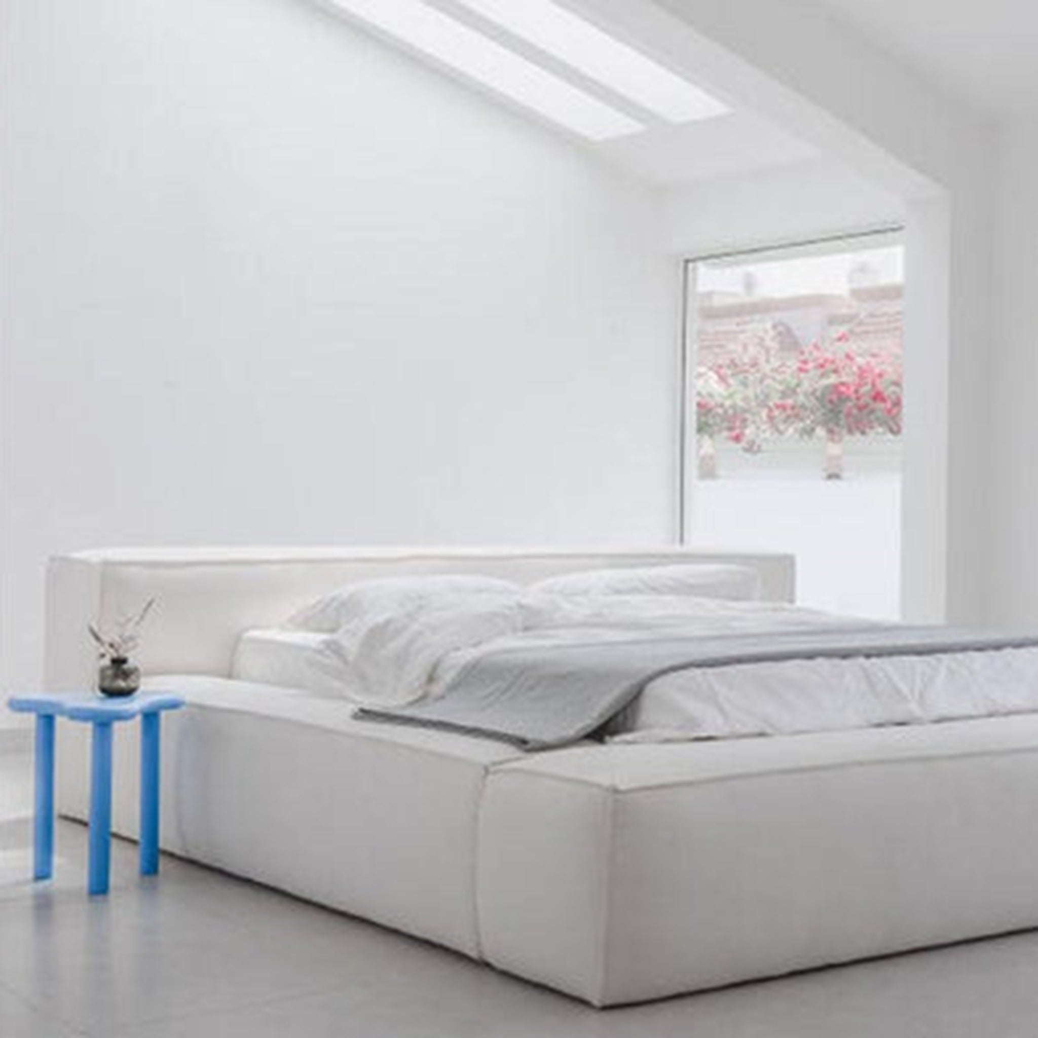 Bright white bed in a minimalist bedroom with a pop of blue. Clean and airy sleeping space.