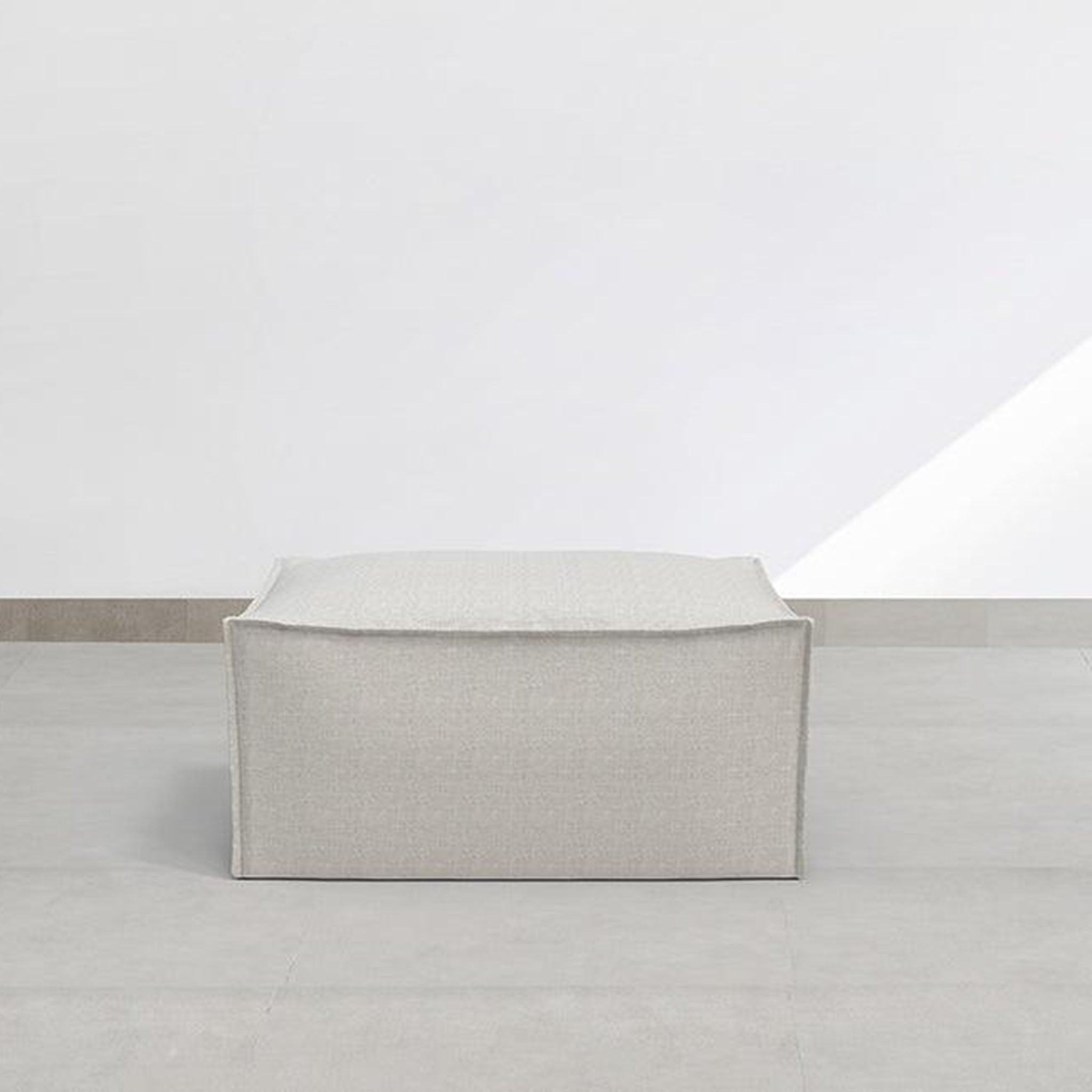Light gray fabric ottoman in a minimalist design, ideal for contemporary living rooms and providing versatile seating or a stylish footrest.