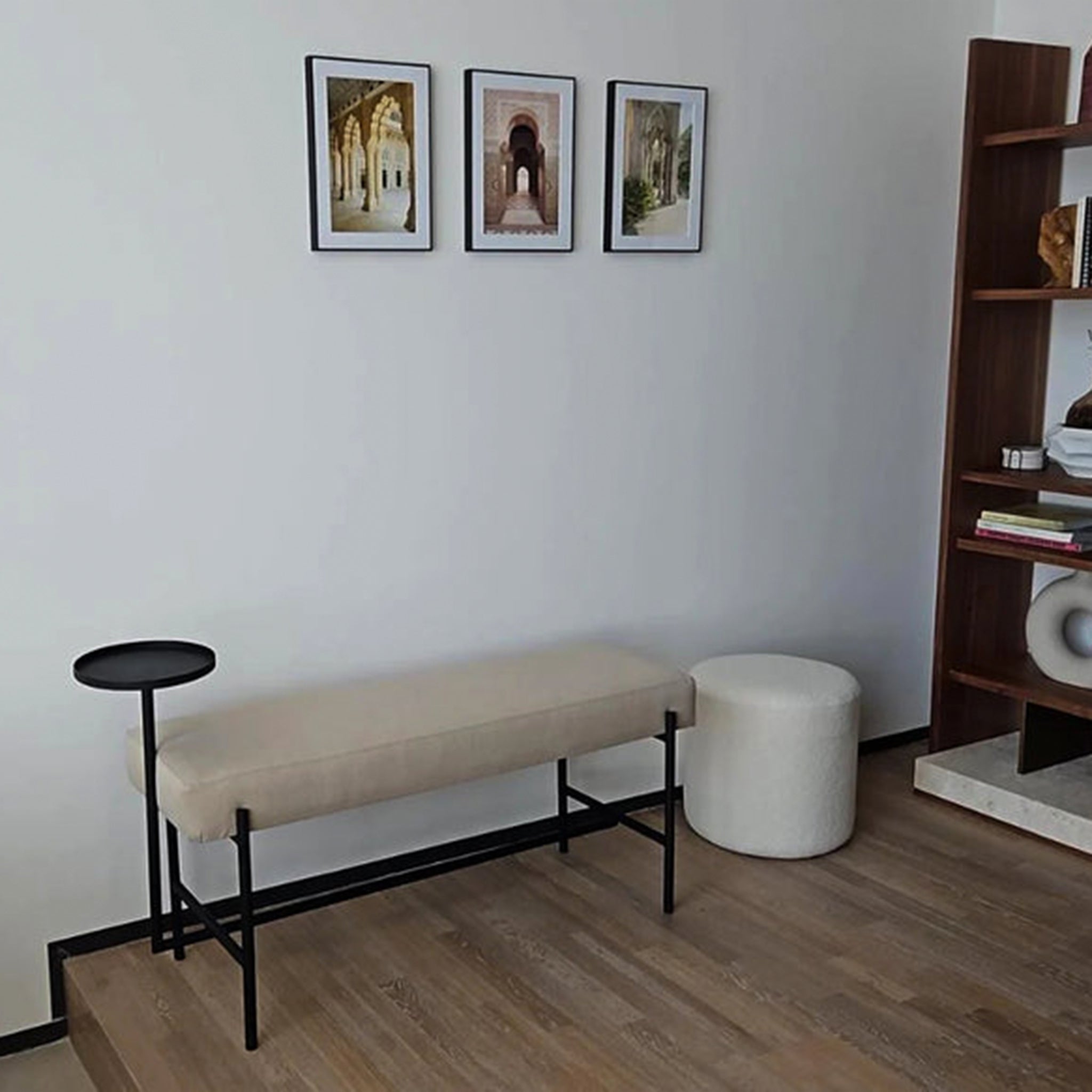 Stylish corner with The Danielle Bench, featuring a beige upholstered seat, black powder-coated steel frame, and an attached side table, accented by framed artwork and a modern bookshelf