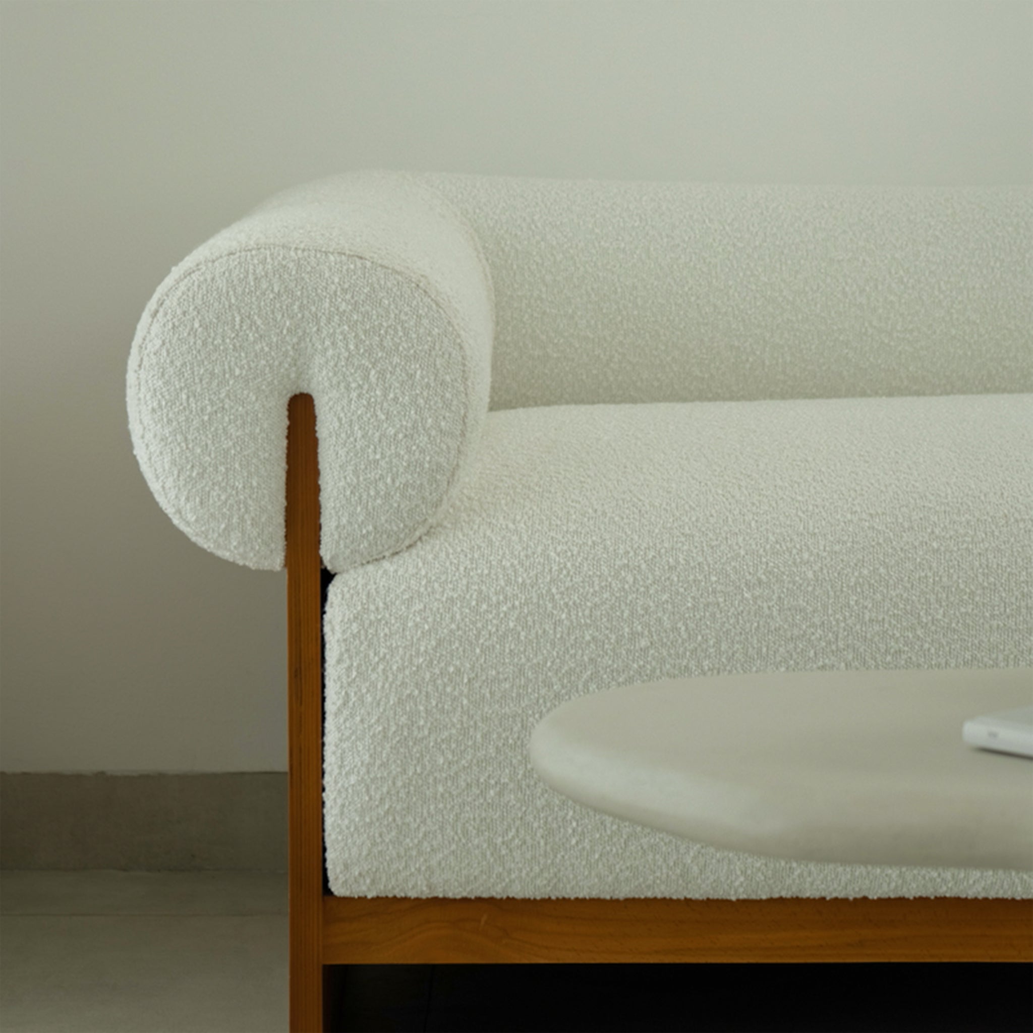 Close-up view of The Devon Chaise featuring its white textured upholstery and wooden frame, highlighting the rolled armrest and modern design elements in a minimalist interior setting.