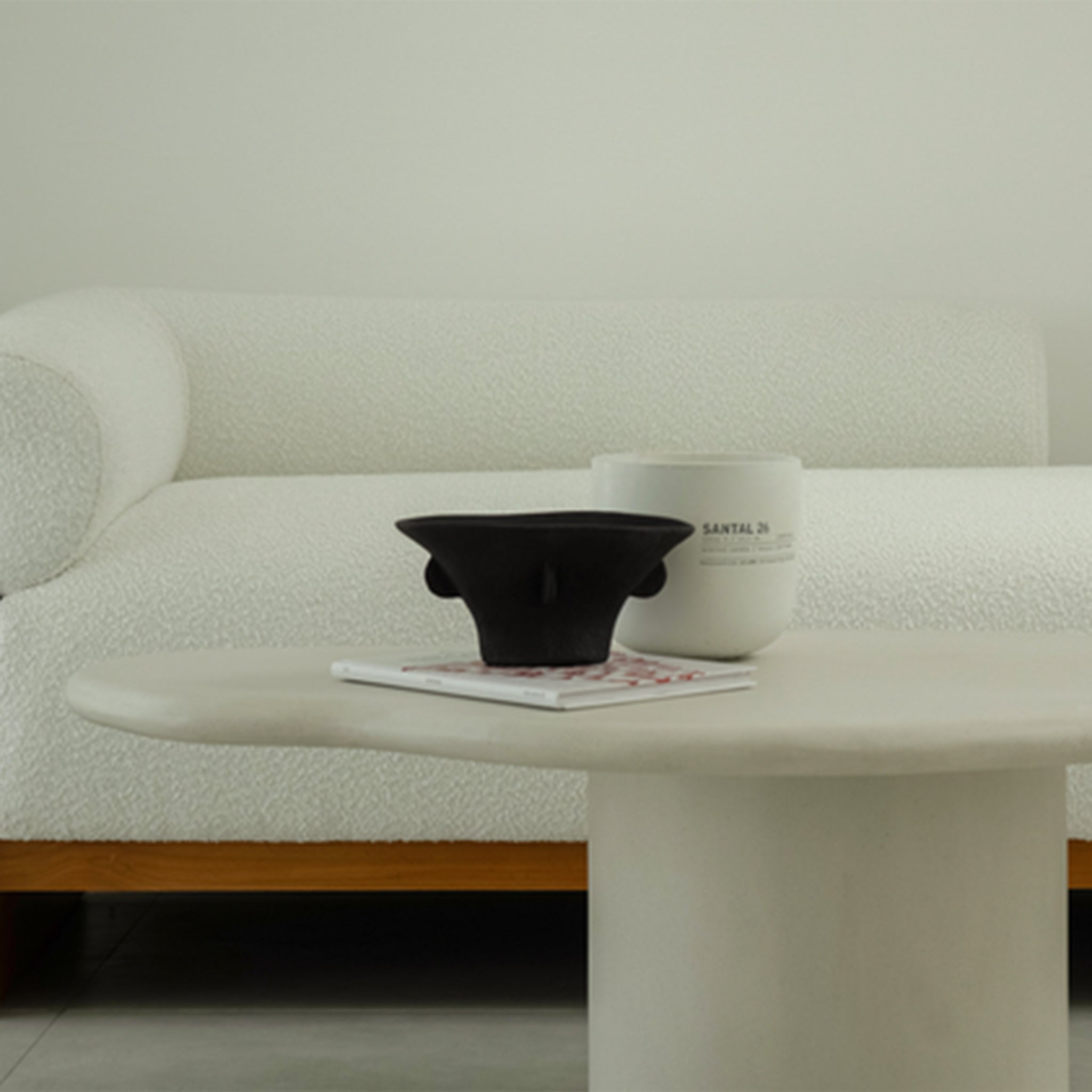 Close-up of The Devon Chaise with white textured upholstery and wooden frame, paired with a modern white coffee table featuring a black bowl and a candle.