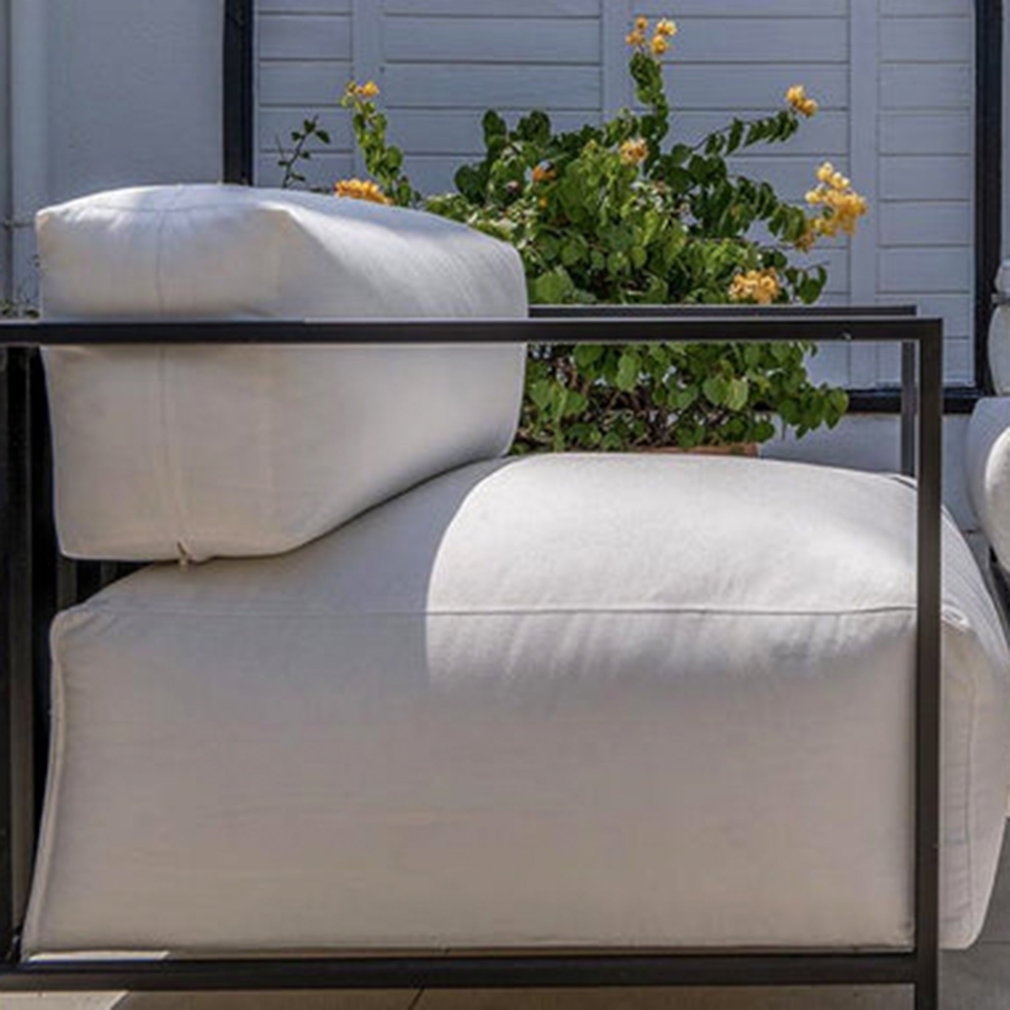 Close-up of The Dexter Accent Chair with plush white cushions and a black metal frame, set against a backdrop of vibrant outdoor greenery.