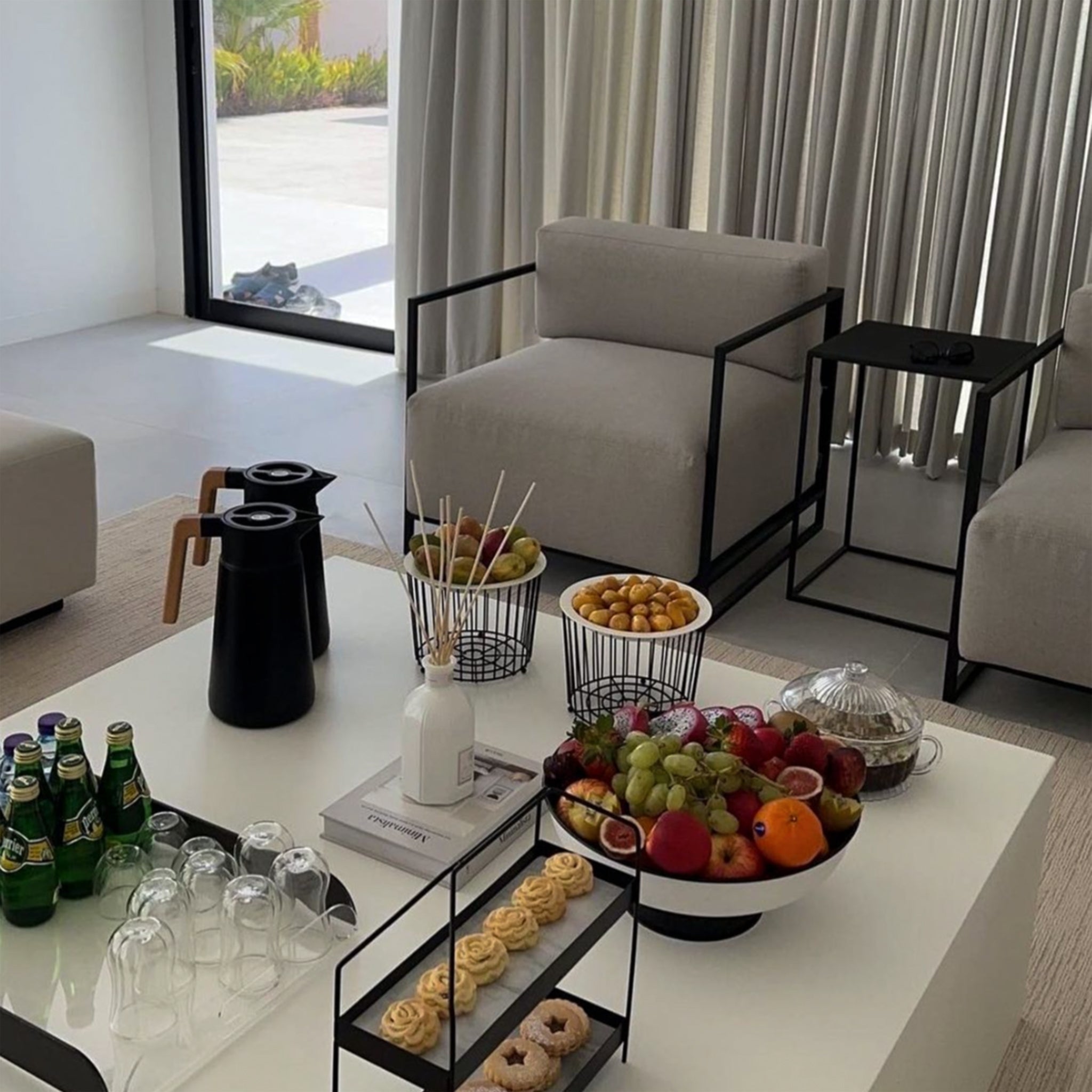 Modern living room setup featuring The Dexter Accent Chairs with light grey cushions and black metal frames, accompanied by a coffee table adorned with snacks, drinks, and decorative items.