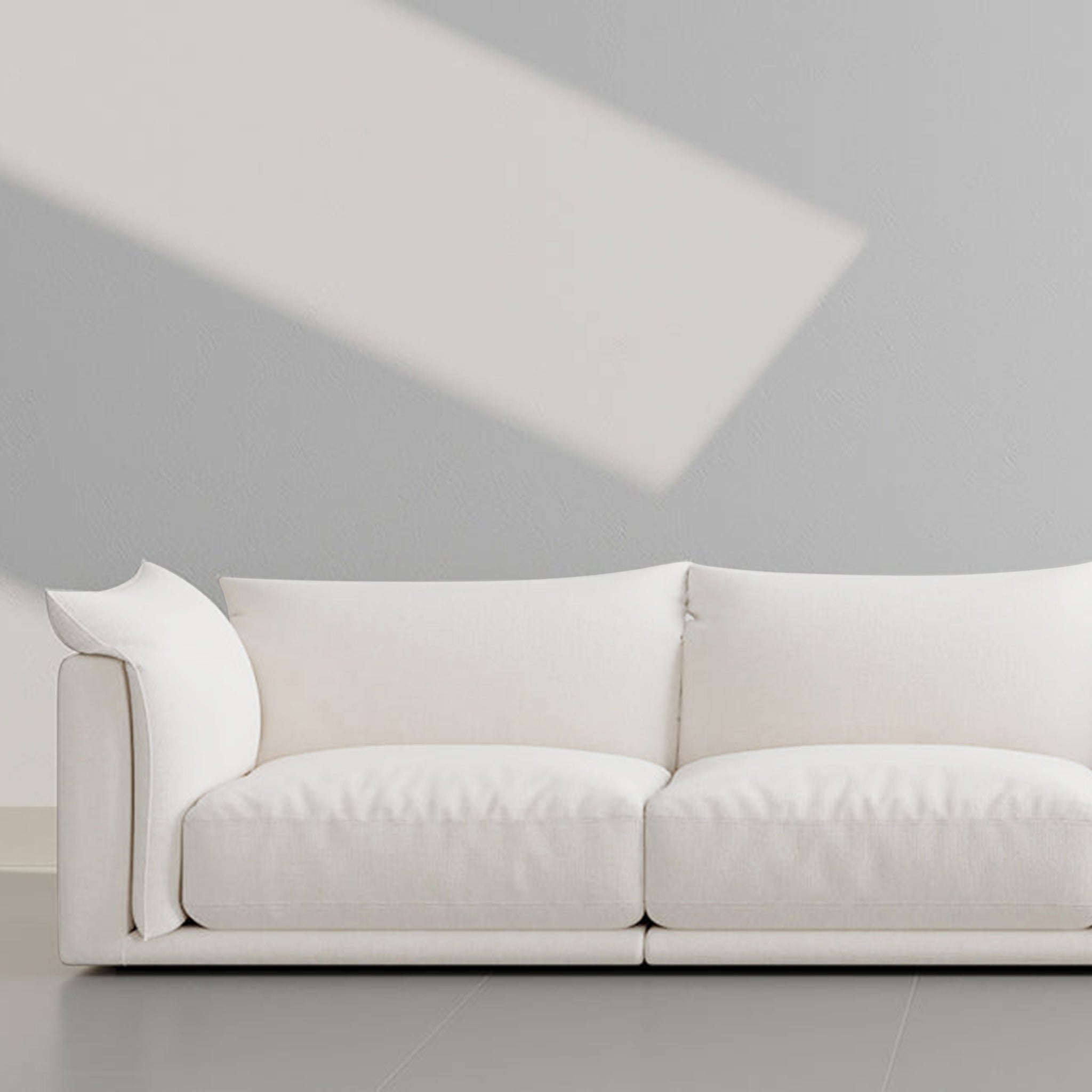 Modern white sofa with plush cushions against a minimalist gray wall, bathed in natural light.