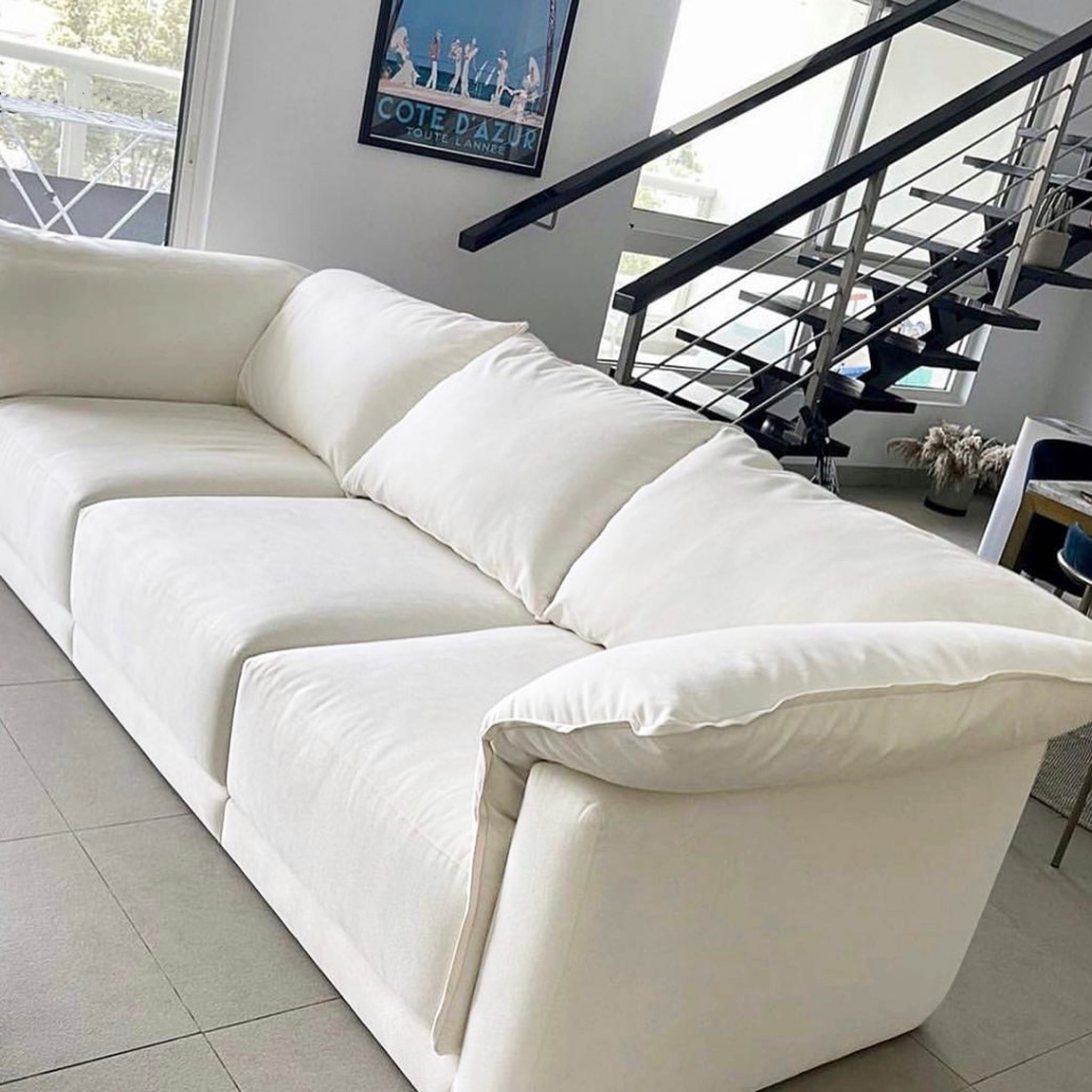 Luxurious white sofa in a modern living room with a sleek black staircase and large windows providing ample natural light.