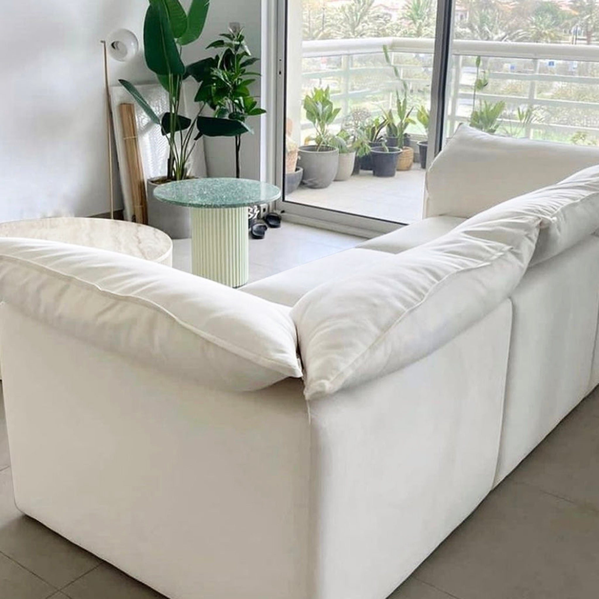 Elegant white sofa in a contemporary living room with large windows leading to a balcony adorned with potted plants.