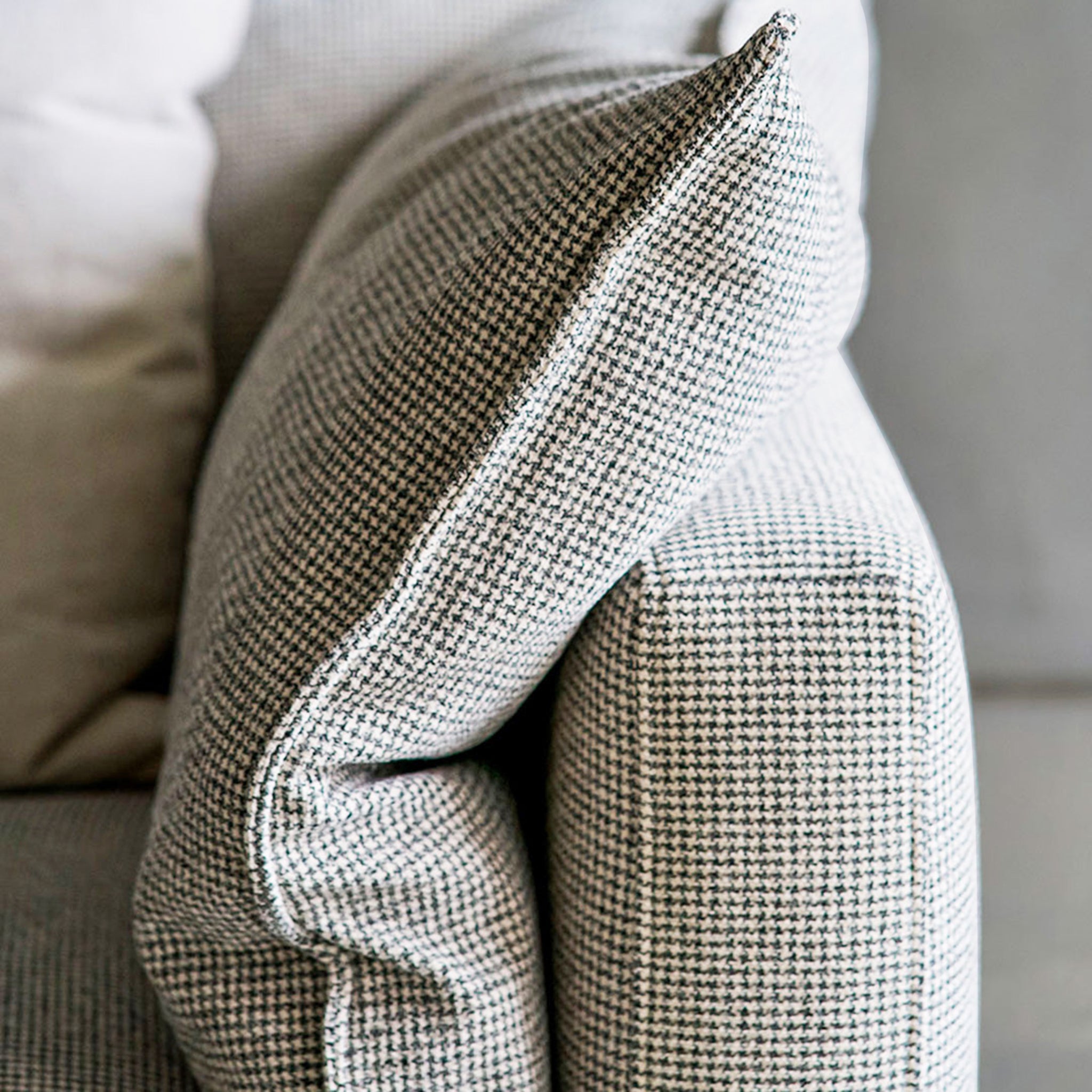 Close-up view of a stylish houndstooth-patterned cushion on a modern sofa, highlighting the fabric texture and detailed stitching for a cozy and elegant living room setup.