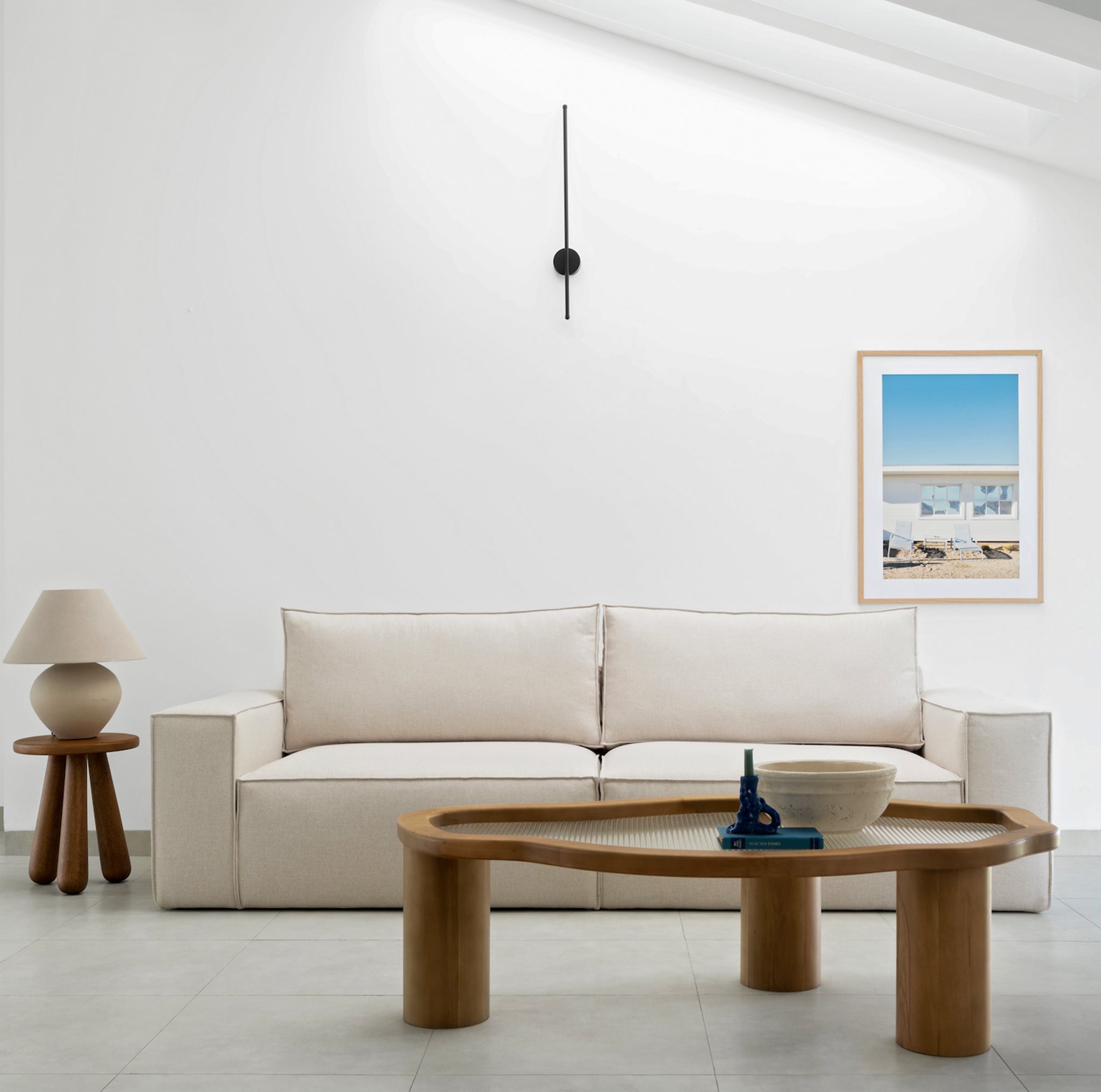 Light and airy living space featuring a comfortable white L-shaped couch, relaxing brown leather ottoman, and a sleek table lamp for a touch of modern design.