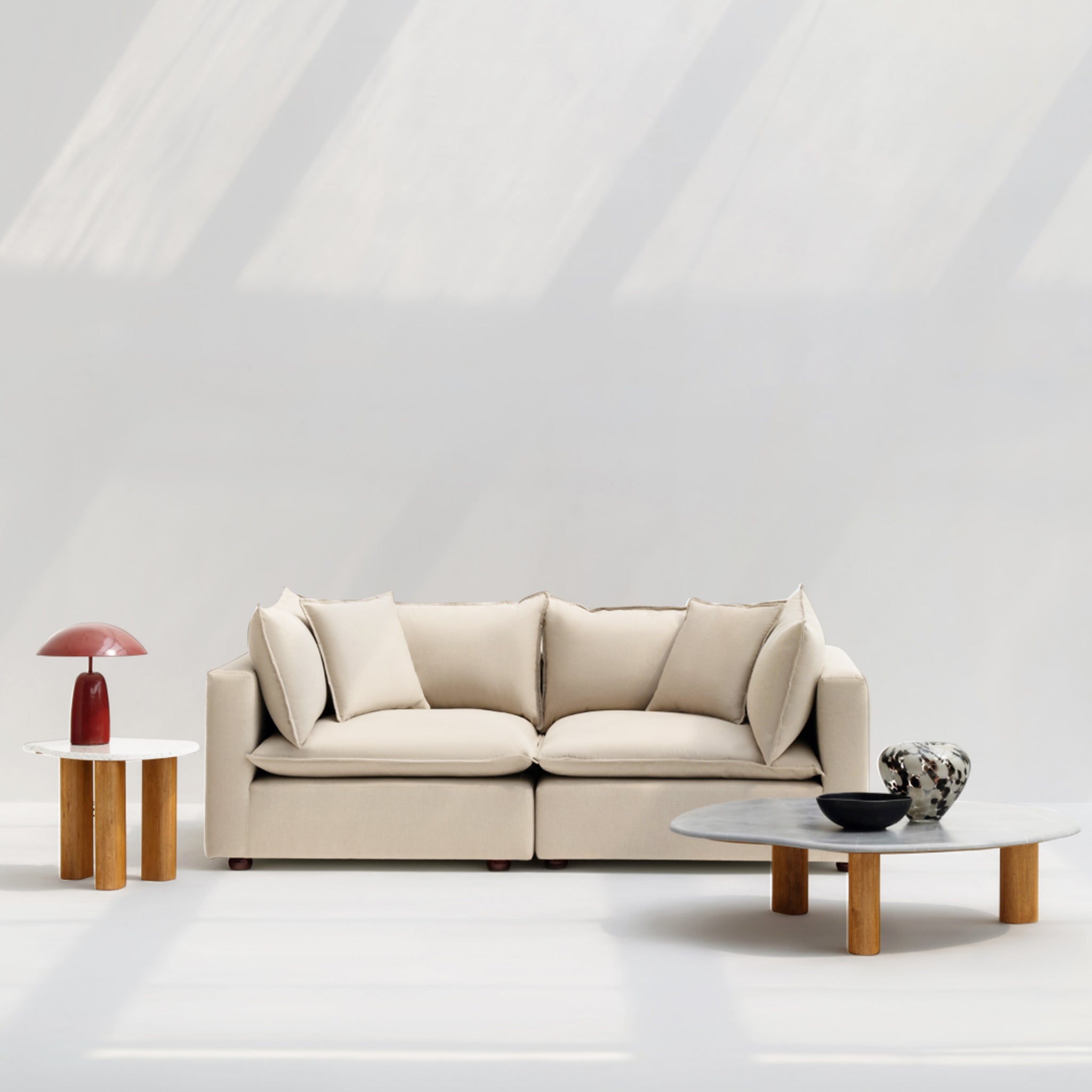 Beige loveseat sofa with soft cushions, styled with modern coffee tables and decorative elements in a bright, minimalist living room.