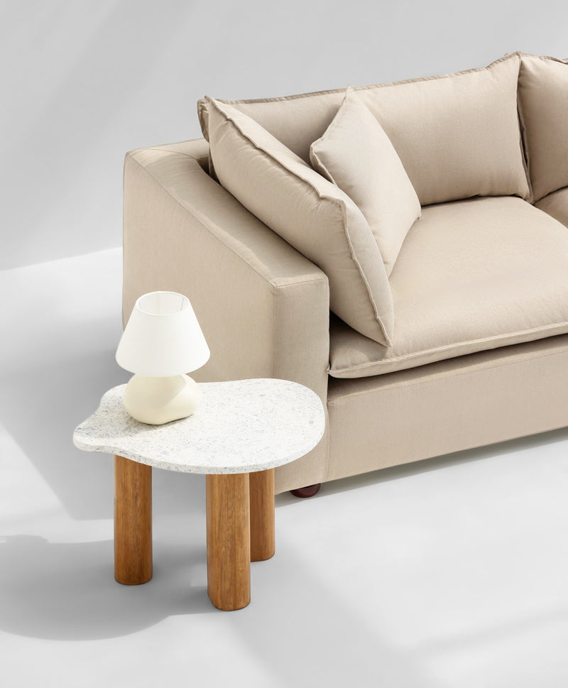 Beige sofa with plush cushions beside a modern, white stone coffee table with wooden legs, creating a cozy and stylish living space.