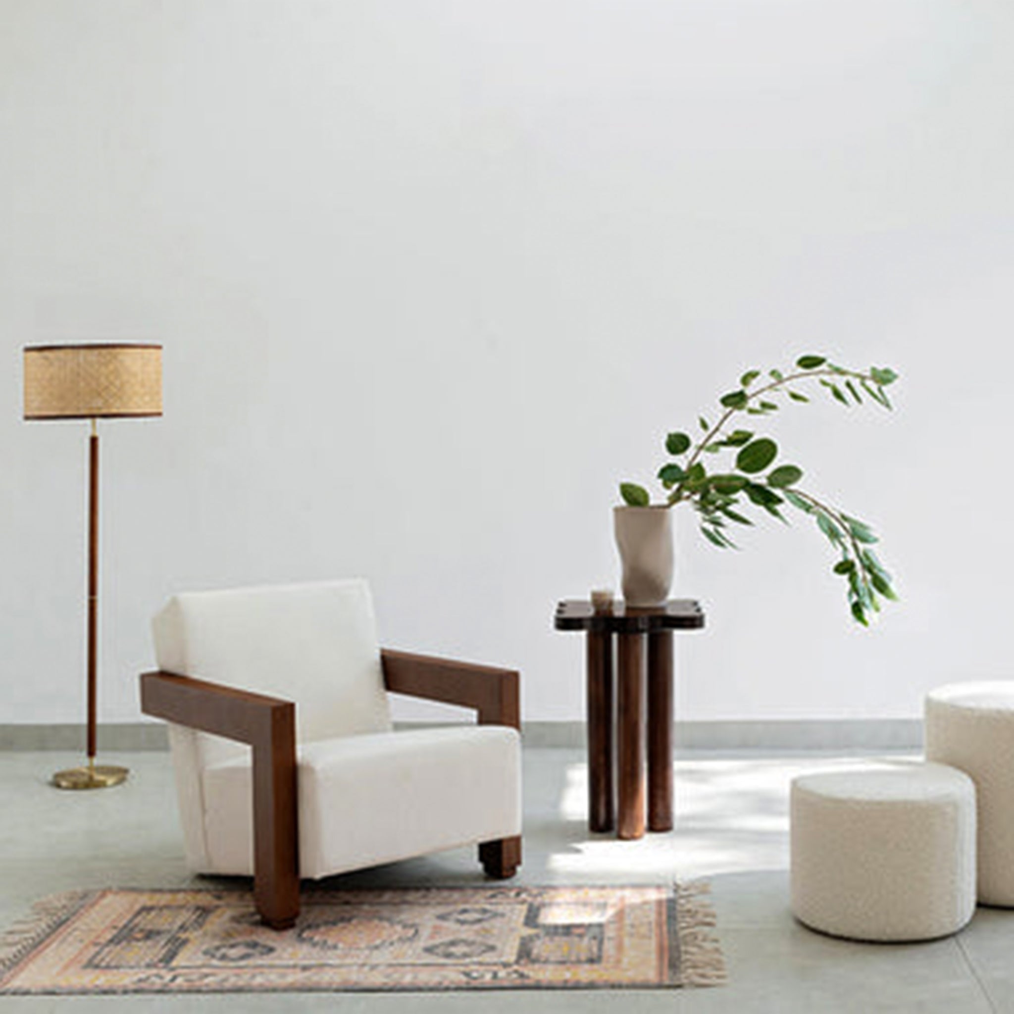 Modern living room setup featuring The Gerrit Accent Chair with white upholstery and wooden armrests, complemented by a floor lamp, a side table with a plant, and a patterned rug.