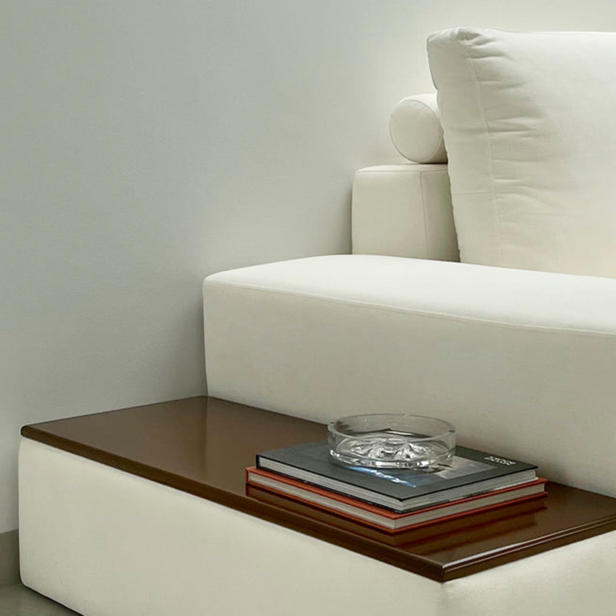 Close-up view of a white sofa with a built-in wooden side table, featuring books and a glass ashtray, showcasing a modern and functional living room design.