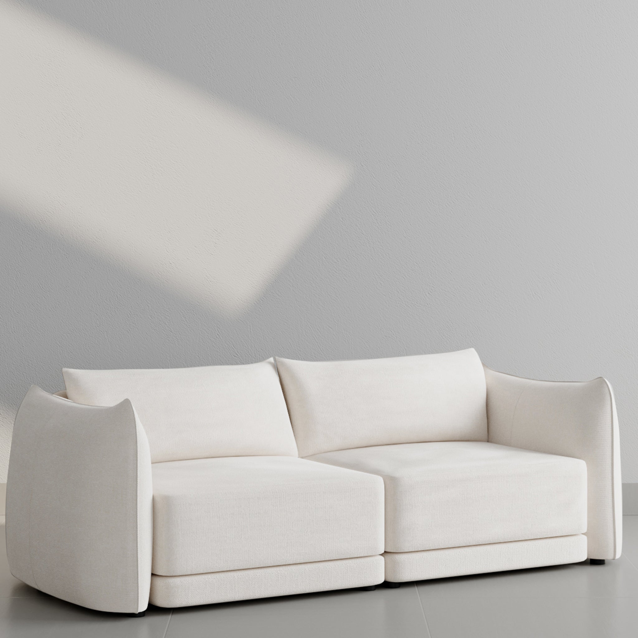 Modern white sofa with curved armrests against a light gray wall, featuring soft cushions and minimalist design.