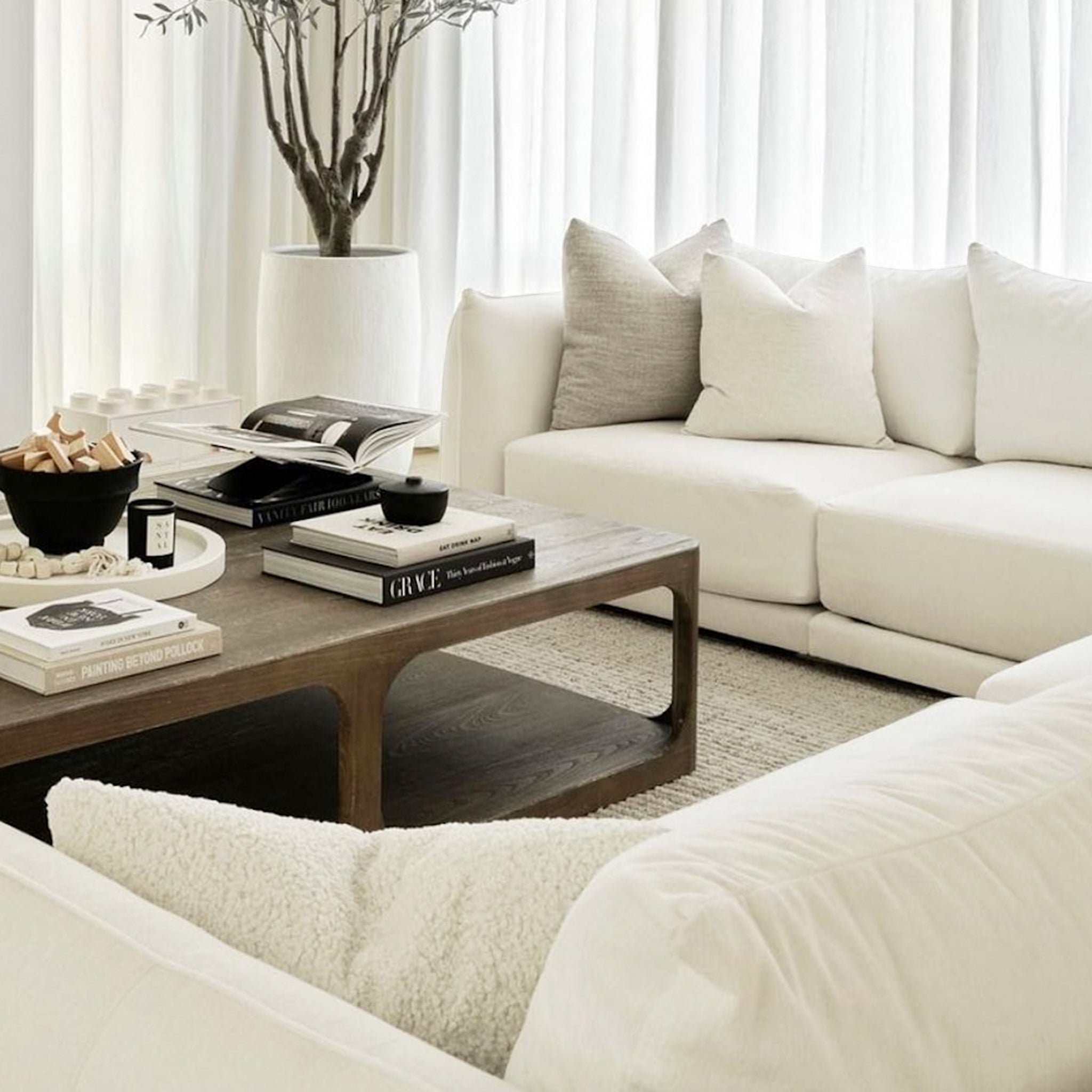 Elegant living room setup featuring a white sectional sofa adorned with cozy pillows, complemented by a wooden coffee table and stylish decor elements.