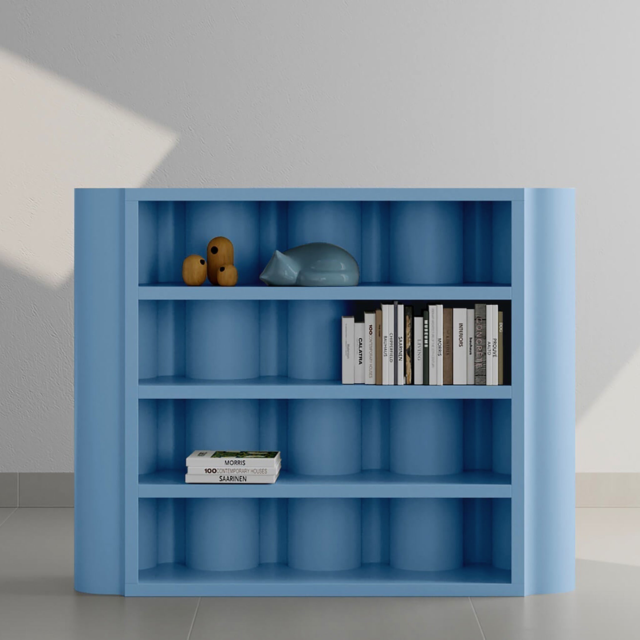 A modern blue bookcase with curved edges, displaying a collection of books and decorative items, including a small sculpture and a ceramic cat figure.