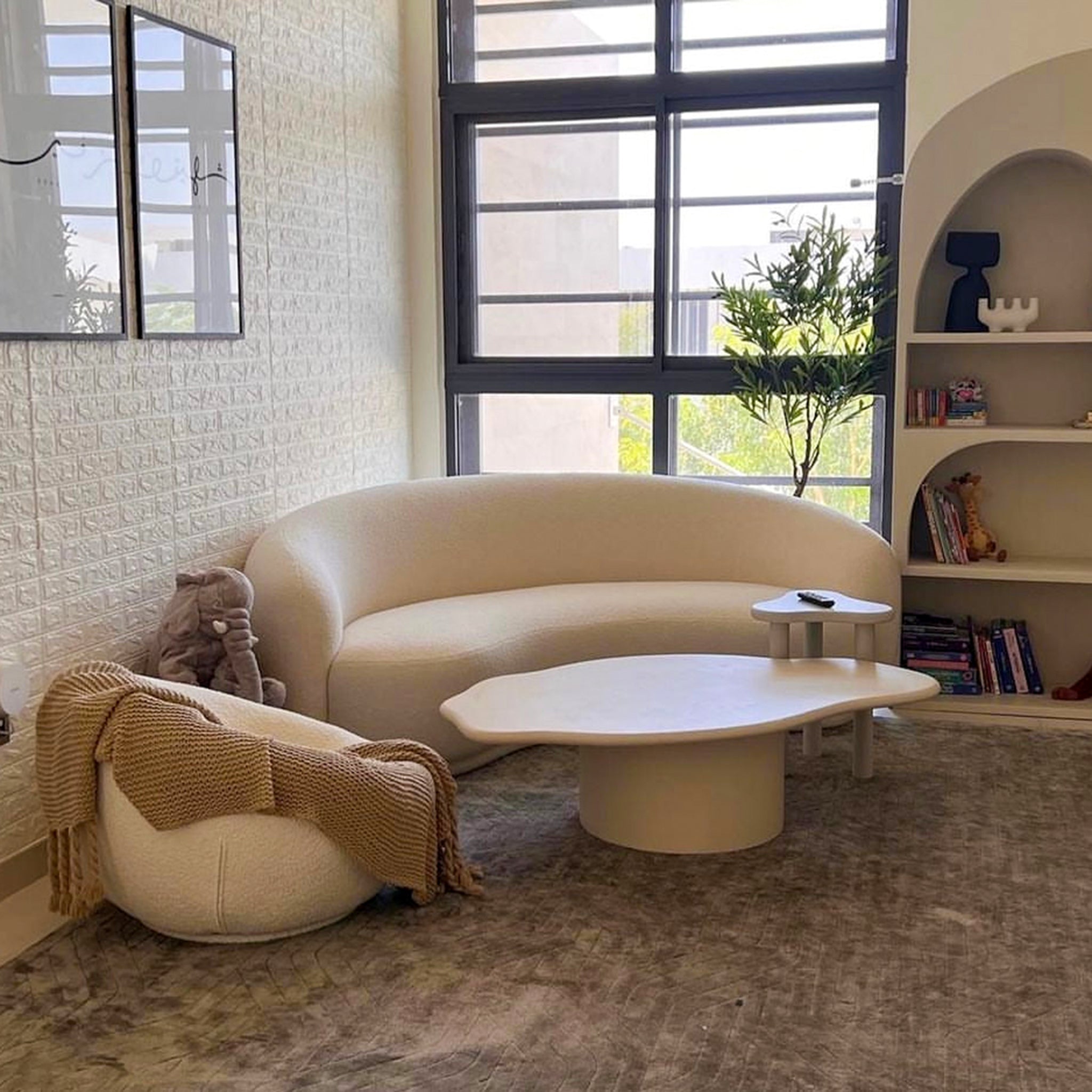 Living room with a white cloud sofa, plush brown ottoman, and round wooden side table for a comfortable and stylish space. 