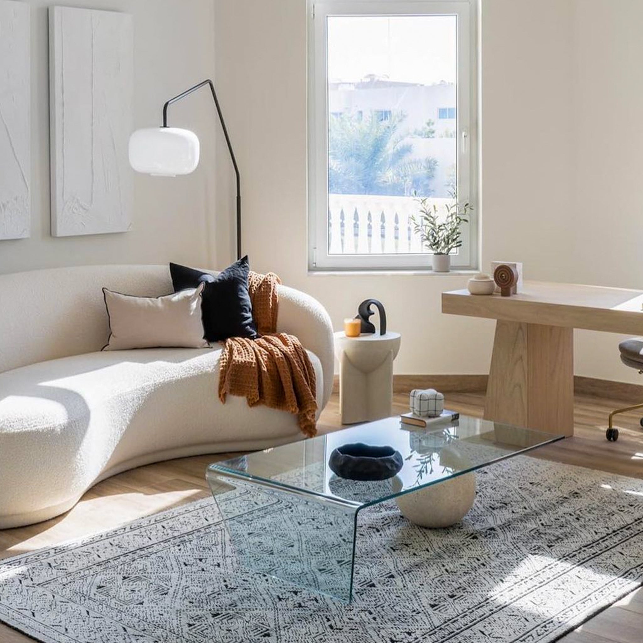 Spacious living room showcasing a plush white L-shaped couch, rich brown leather ottoman, and a sleek wooden side table, perfect for entertaining guests.