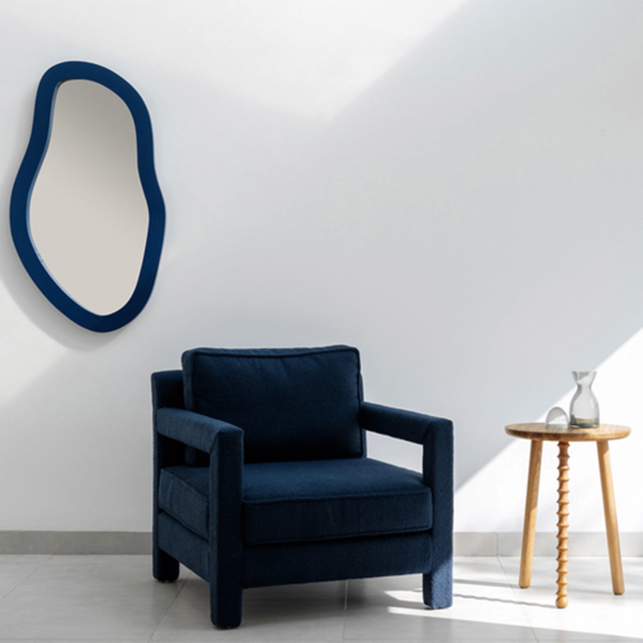 "Modern living room setup featuring The Parsons Accent Chair with deep blue upholstery, a uniquely shaped wall mirror, and a wooden side table with a glass carafe and cup."