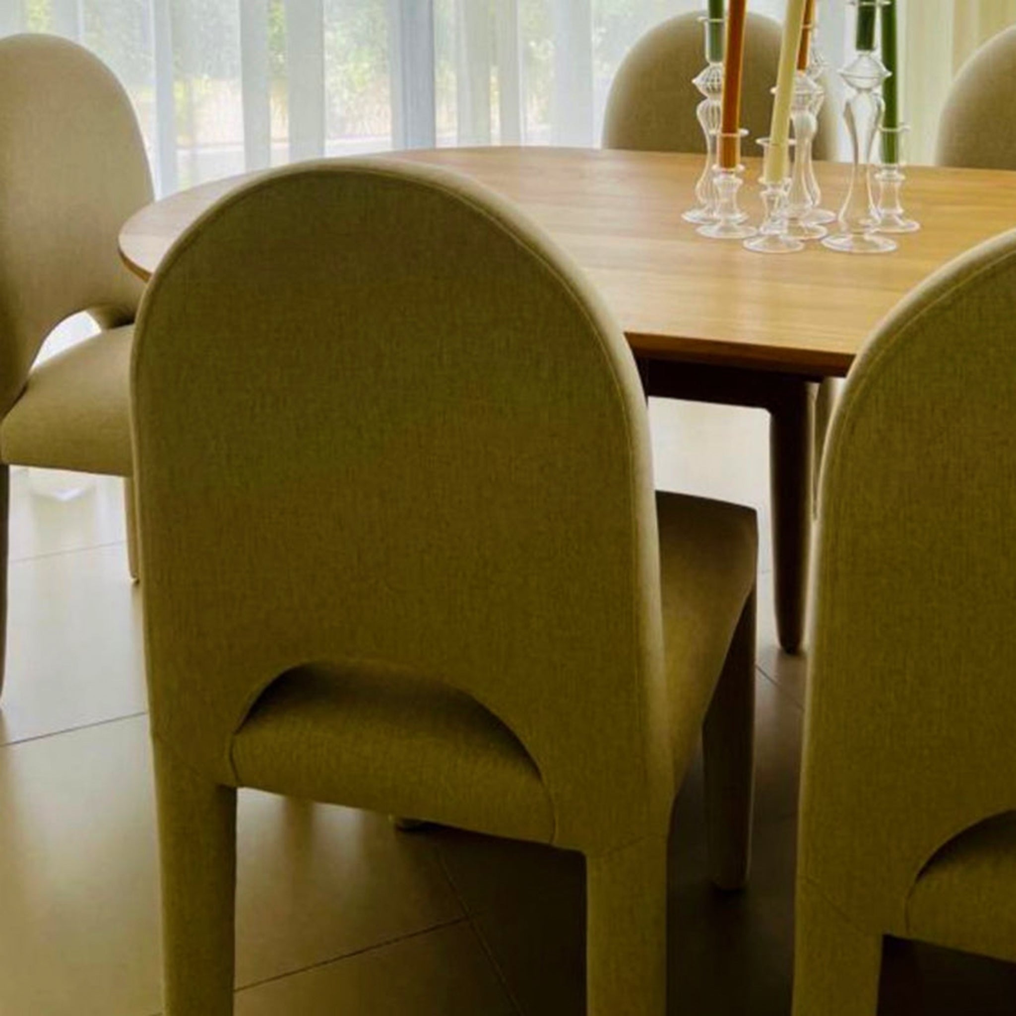 The Shelly Chair - close-up view of modern upholstered dining chairs with curved backs and elegant thin legs around a wooden dining table, decorated with glass candle holders.
