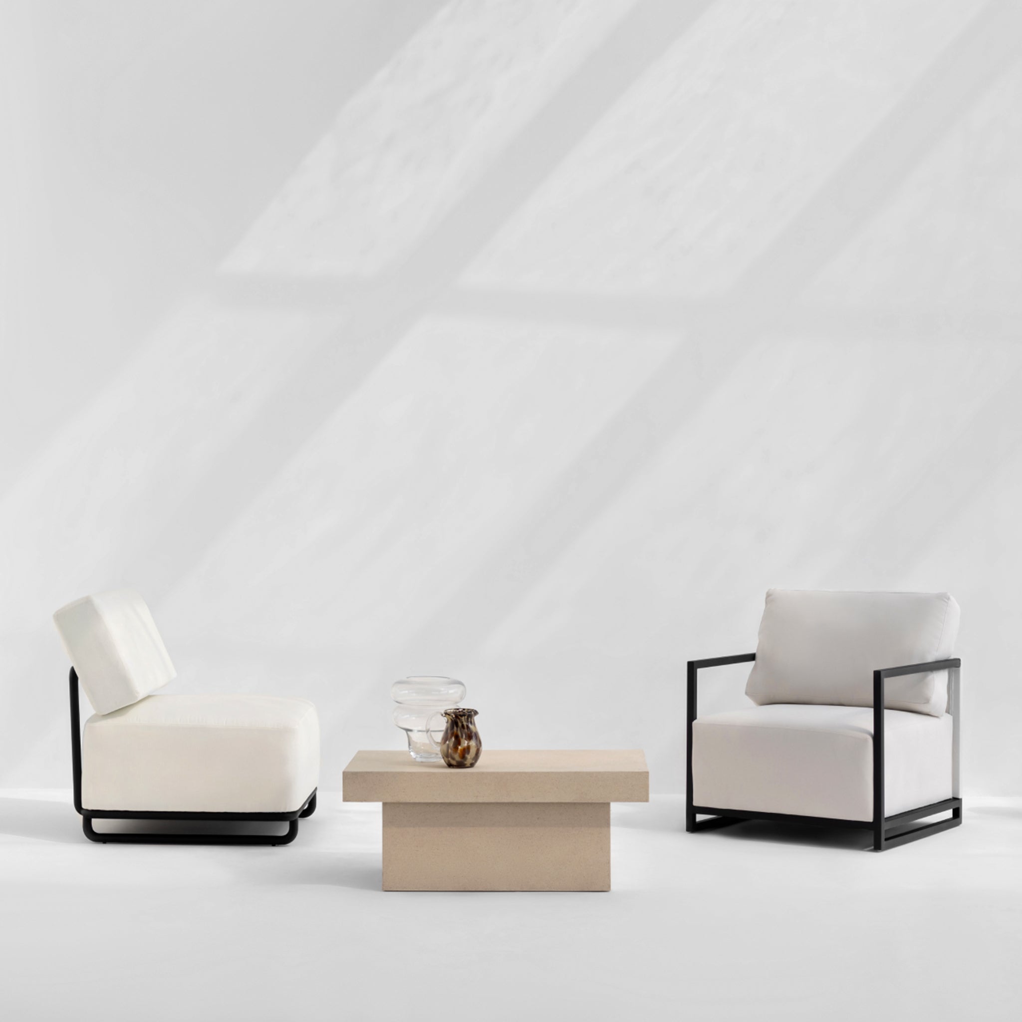 "The Trevor Outdoor Modular Accent Chair in white with sleek black frame, positioned next to a minimalist beige coffee table."