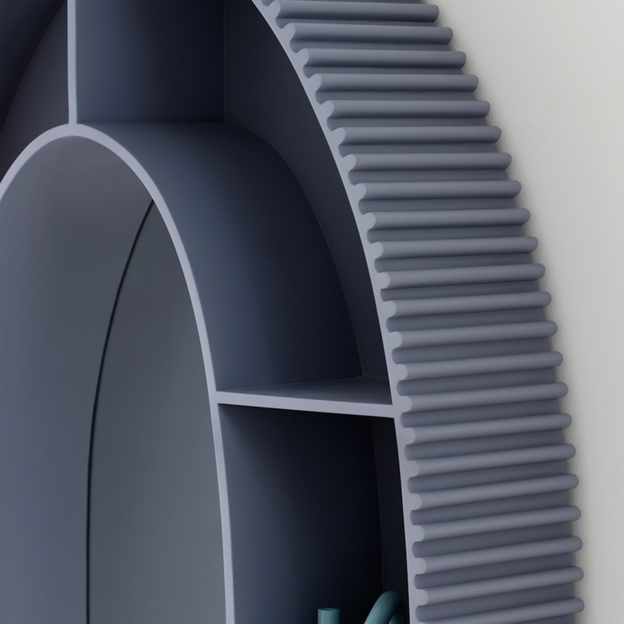 Close-up view of a modern, arch-shaped bookshelf in muted gray, highlighting the grooved edges and a single lit candle on one of the shelves. The bookshelf is positioned against a light gray wall, emphasizing its sleek and contemporary design.