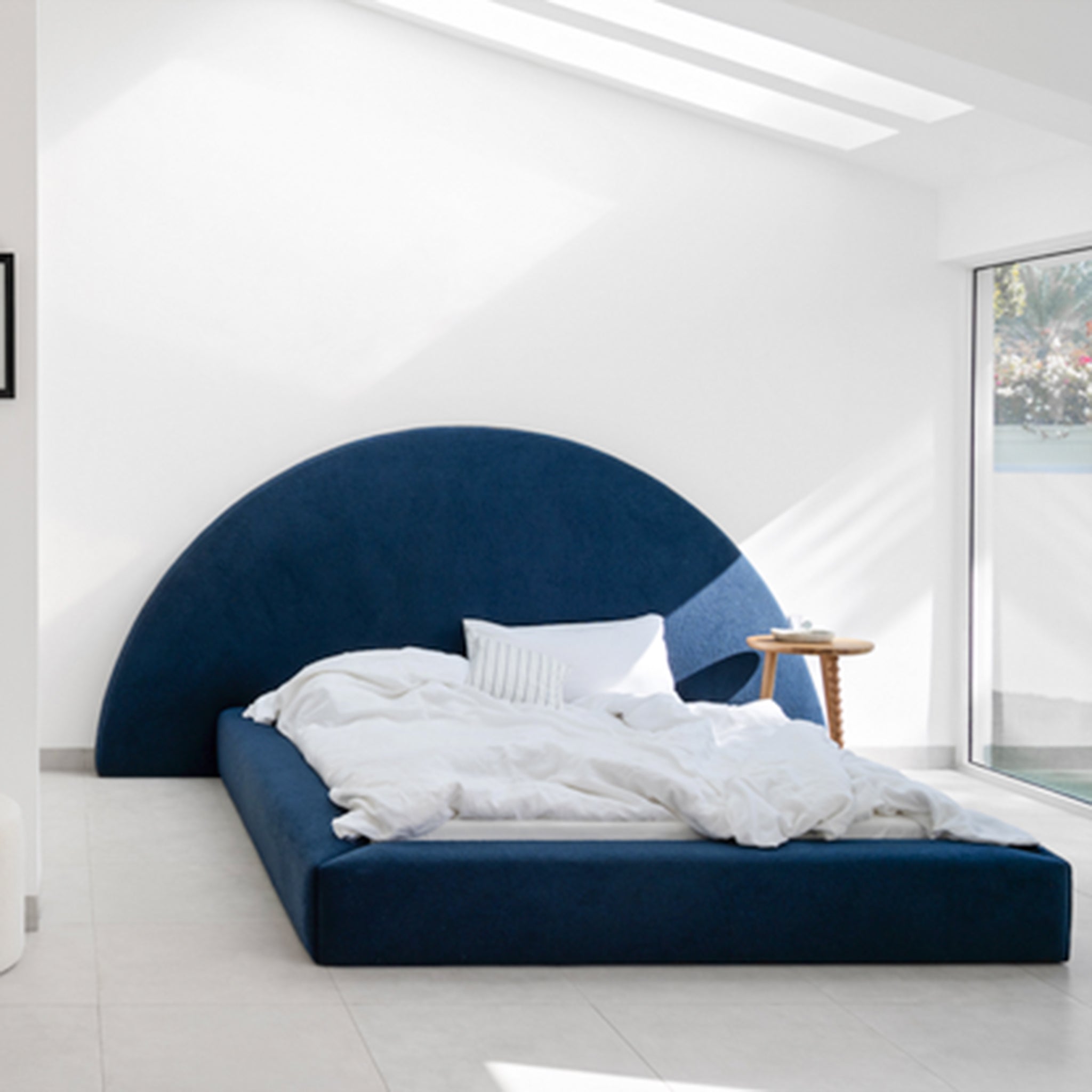Blue upholstered bed with a large semi-circular headboard and a low profile frame. This luxurious bed is perfect for a stylish and sophisticated bedroom.