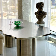 The Victoria steel dining table in a stylish living space, showcasing its curvy design and stainless steel finish.