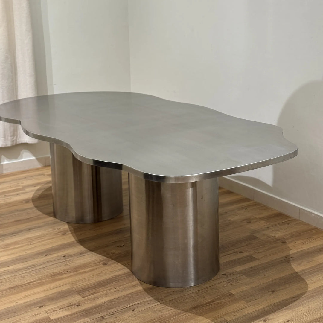 Stylish steel dining table with a reflective stainless steel top, placed in a spacious and chic dining area.